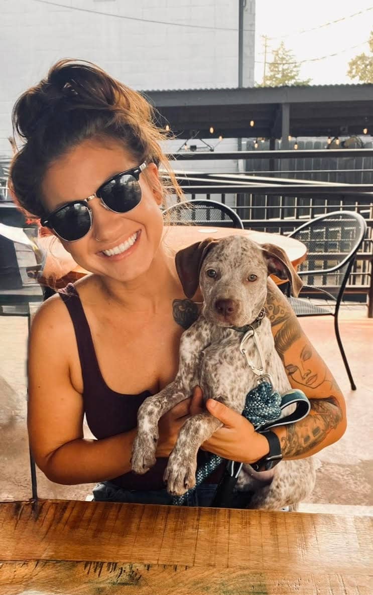 Kayla Parker, RN, BSN, a surgical trauma ICU nurse, smiles while wearing sunglasses and holding a dog.
