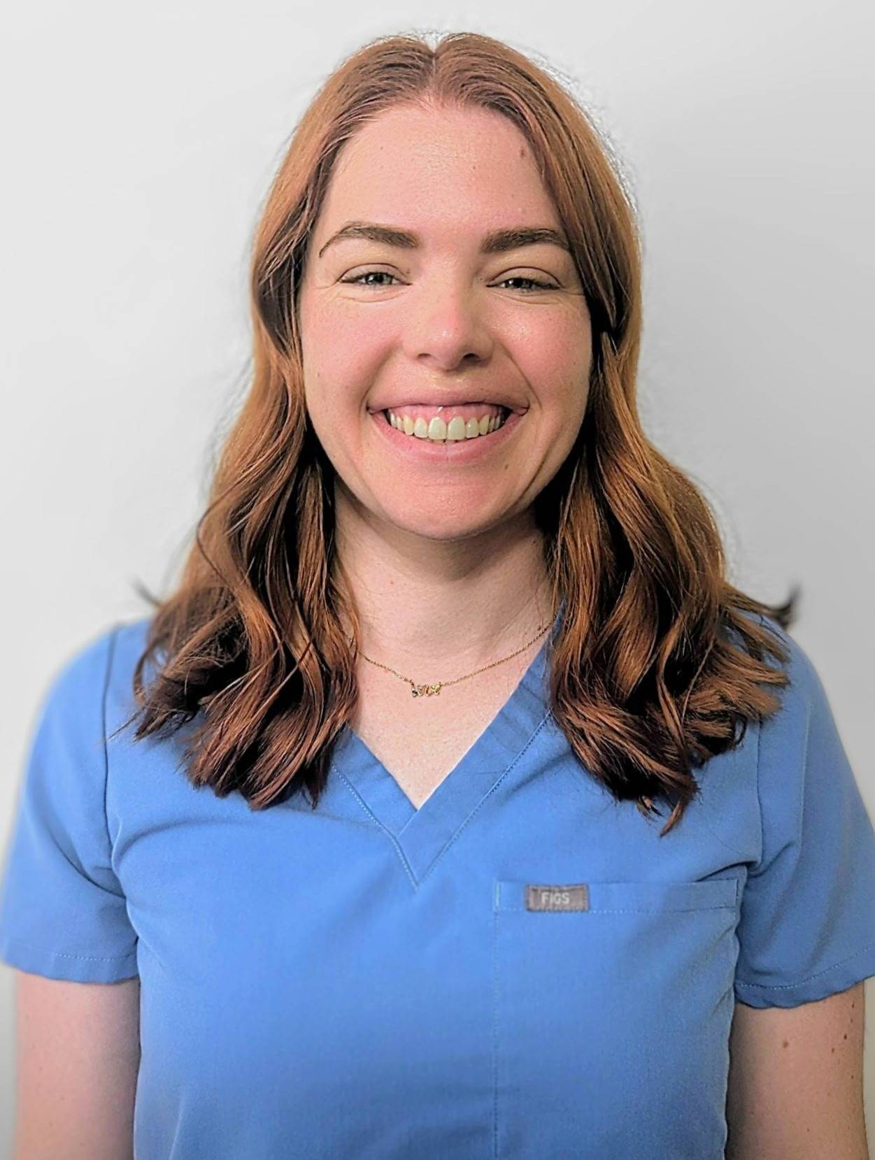 Sarah Balcom, RN, BSN, smiles while wearing blue scrubs in a headshot.