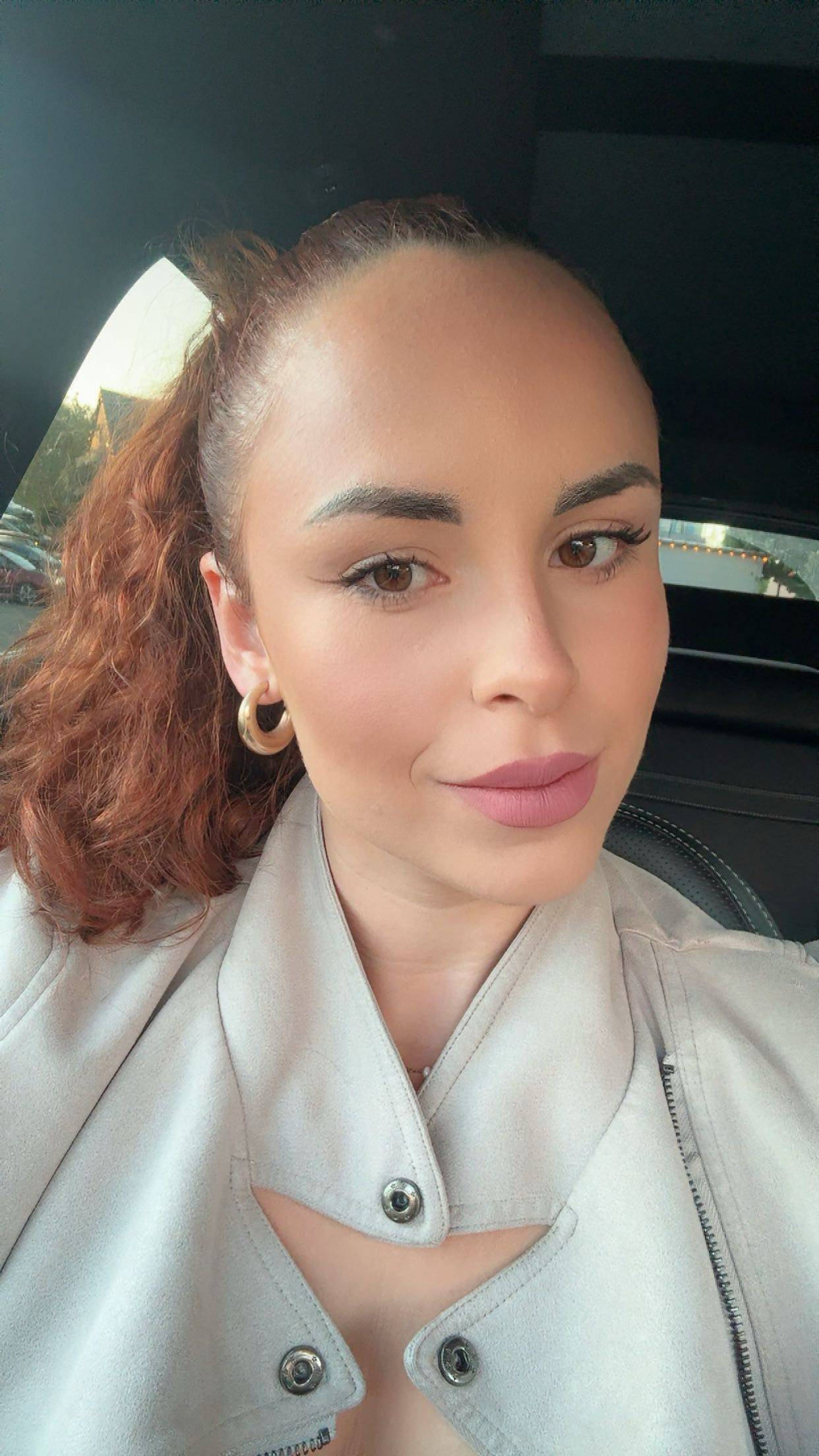 Headshot of a woman with curly hair, wearing a beige coat.