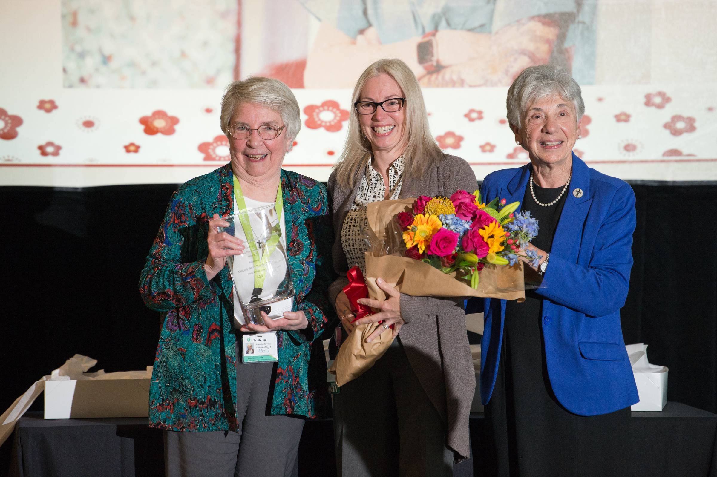 Kimberly Wade, BSN, RN, CNOR, a clinical educator stands with two other women while holding flowers.