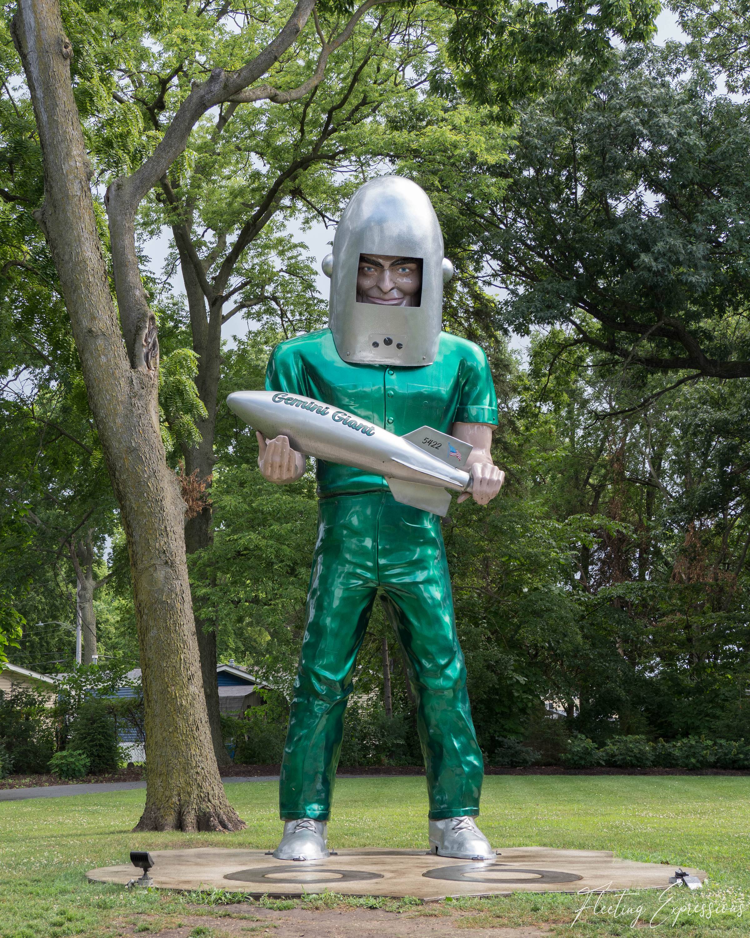 A green muffler man statue named Gemini Giant holds a silver rocket labeled 5422 among leafy trees in Wilmington, Illinois.