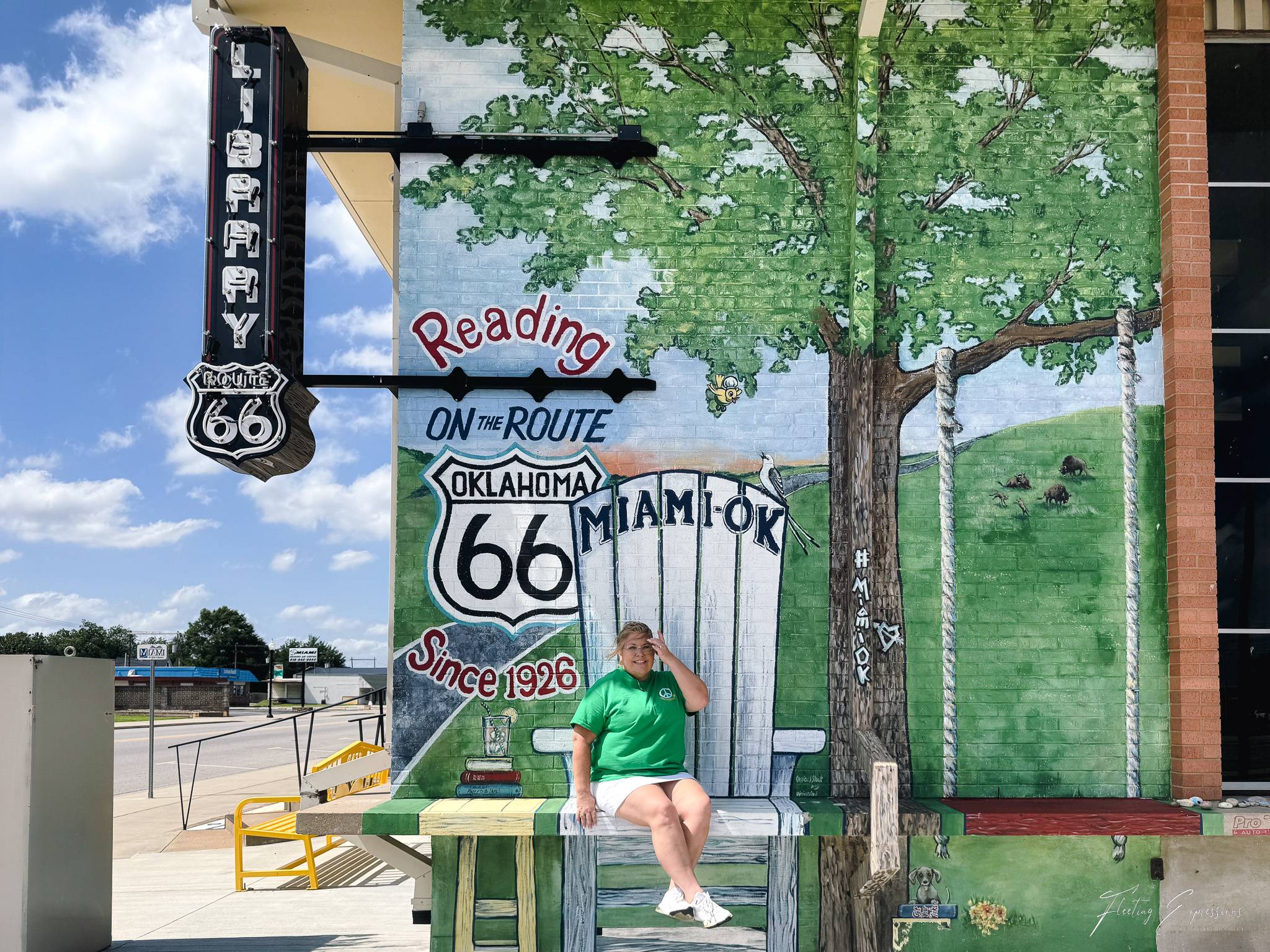 Colorful Route 66 mural on the Miami Public Library featuring a large white Adirondack chair, leafy tree, swing, and "Reading on the Route" artwork.