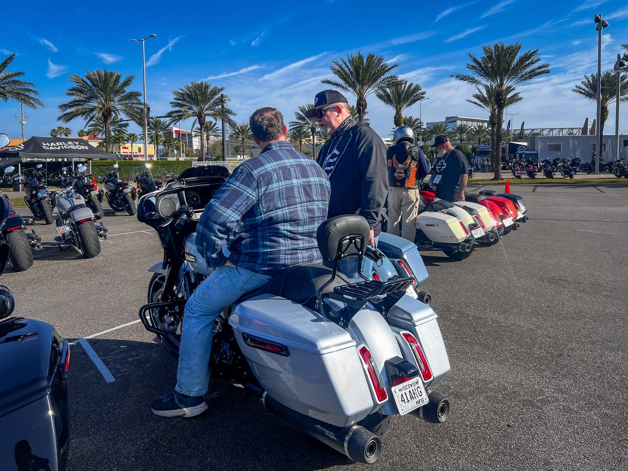 person sitting on motorcycle talking to standing person in a parking lot with palm trees in background