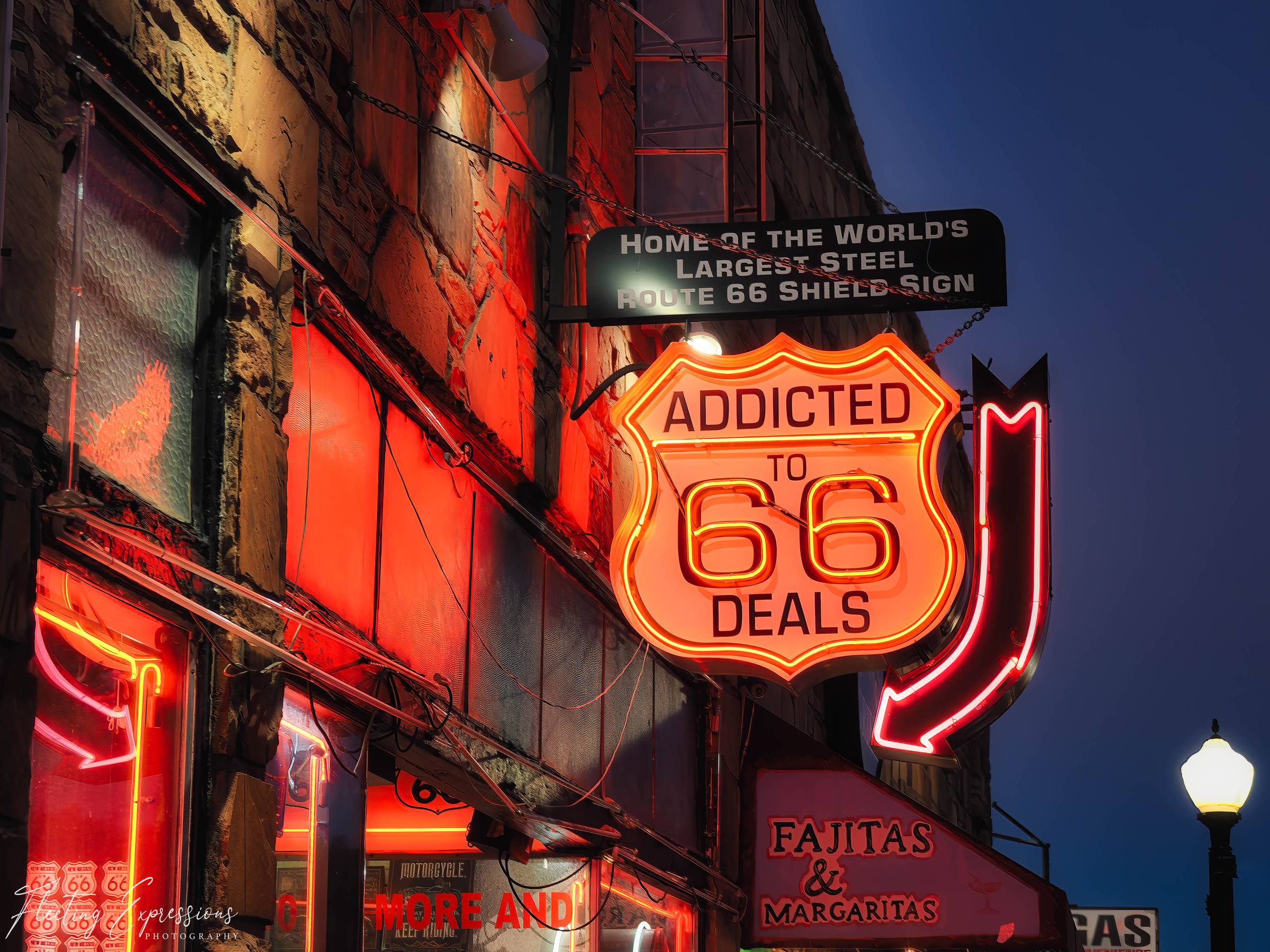 Bright neon Route 66 sign glowing red and orange outside a downtown Flagstaff building at night.