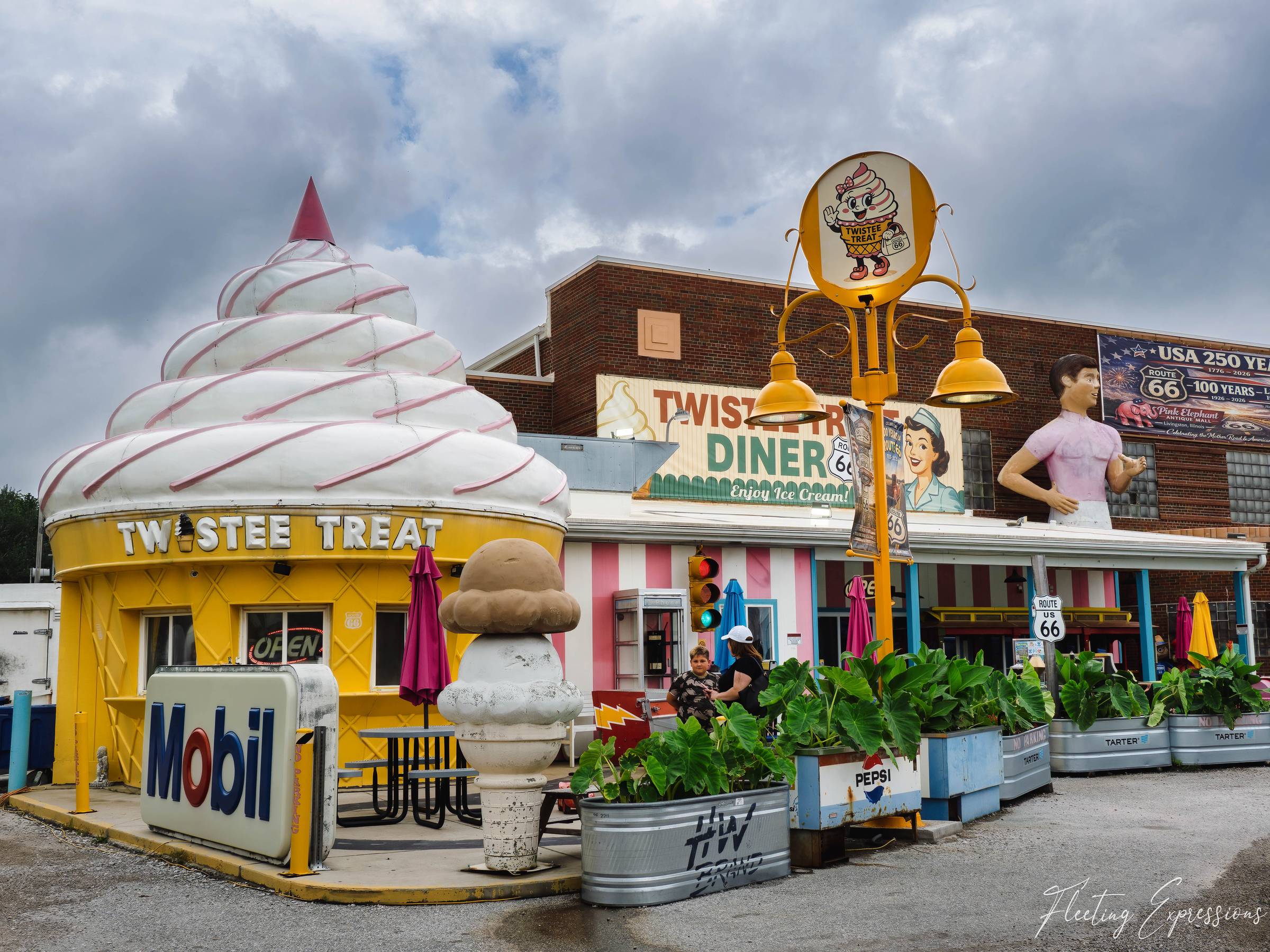A yellow ice cream cone-shaped building labeled "Twistee Treat" beside a pink-striped diner storefront, with a giant Muffler Man statue in a pink shirt visible behind.