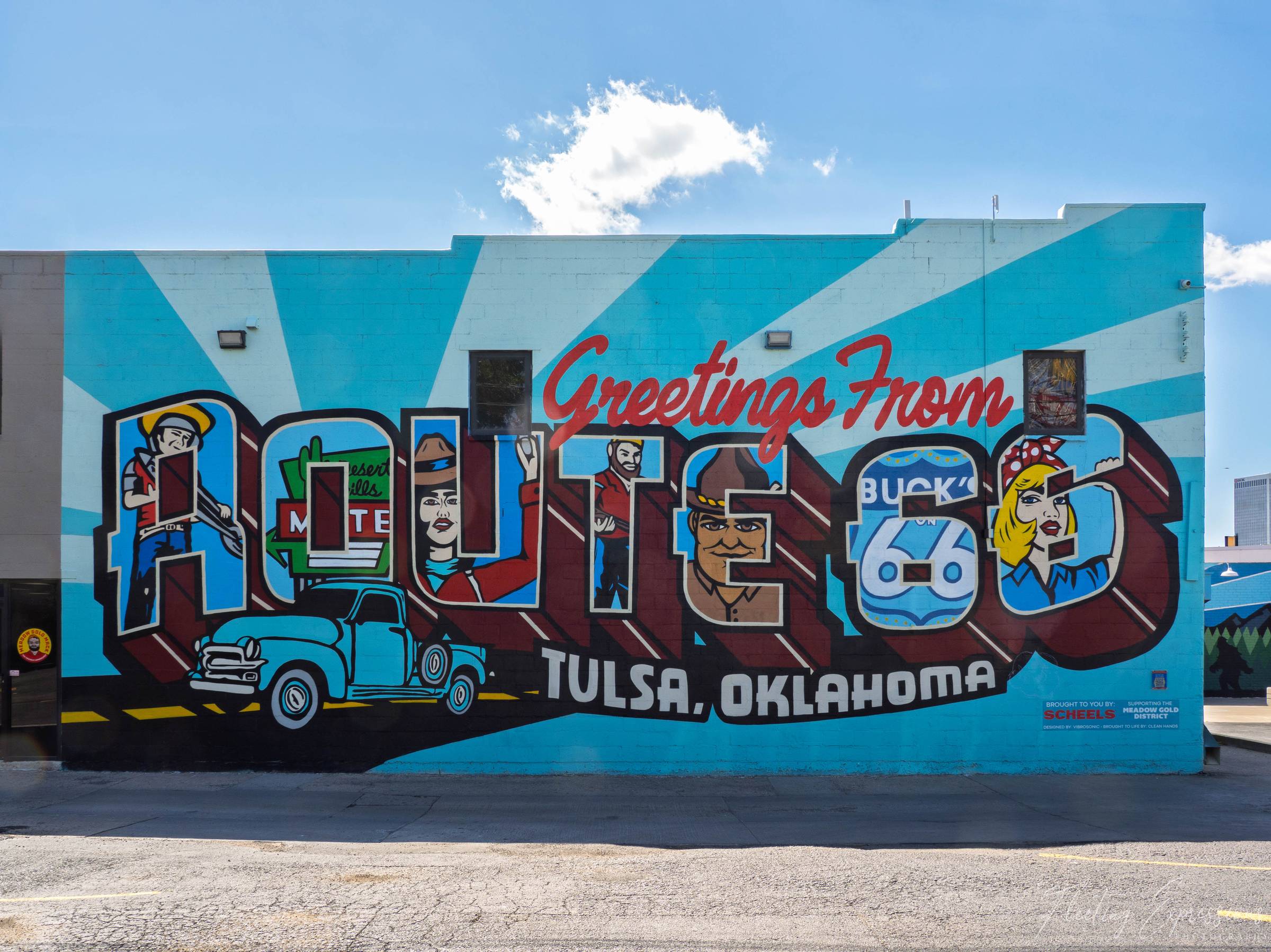A bright mural reads “Greetings From Route 66, Tulsa, Oklahoma” with cartoon figures and a blue pickup truck filling the block letters. 