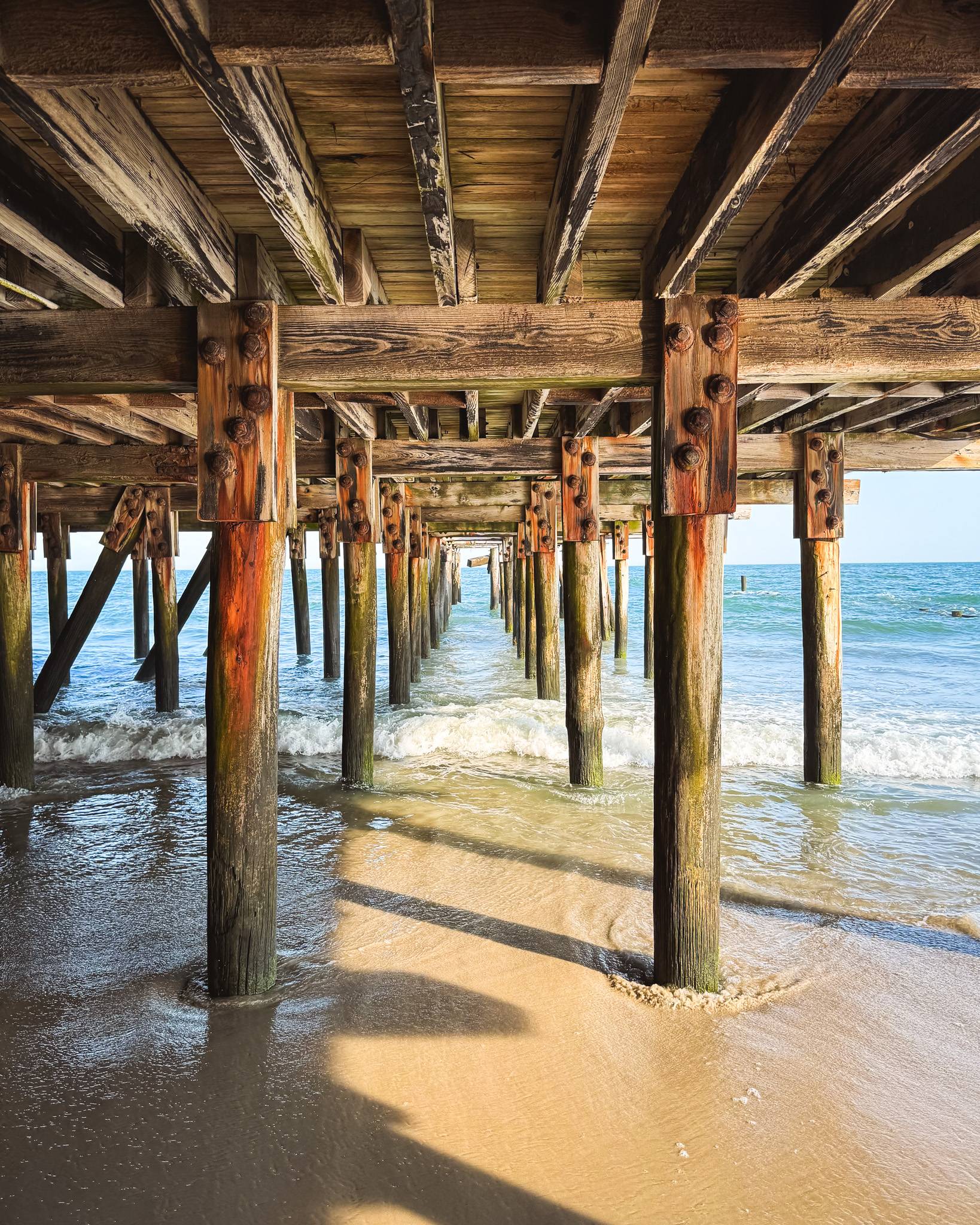 view from under pier looking out to ocean as waves crashing into pier 
