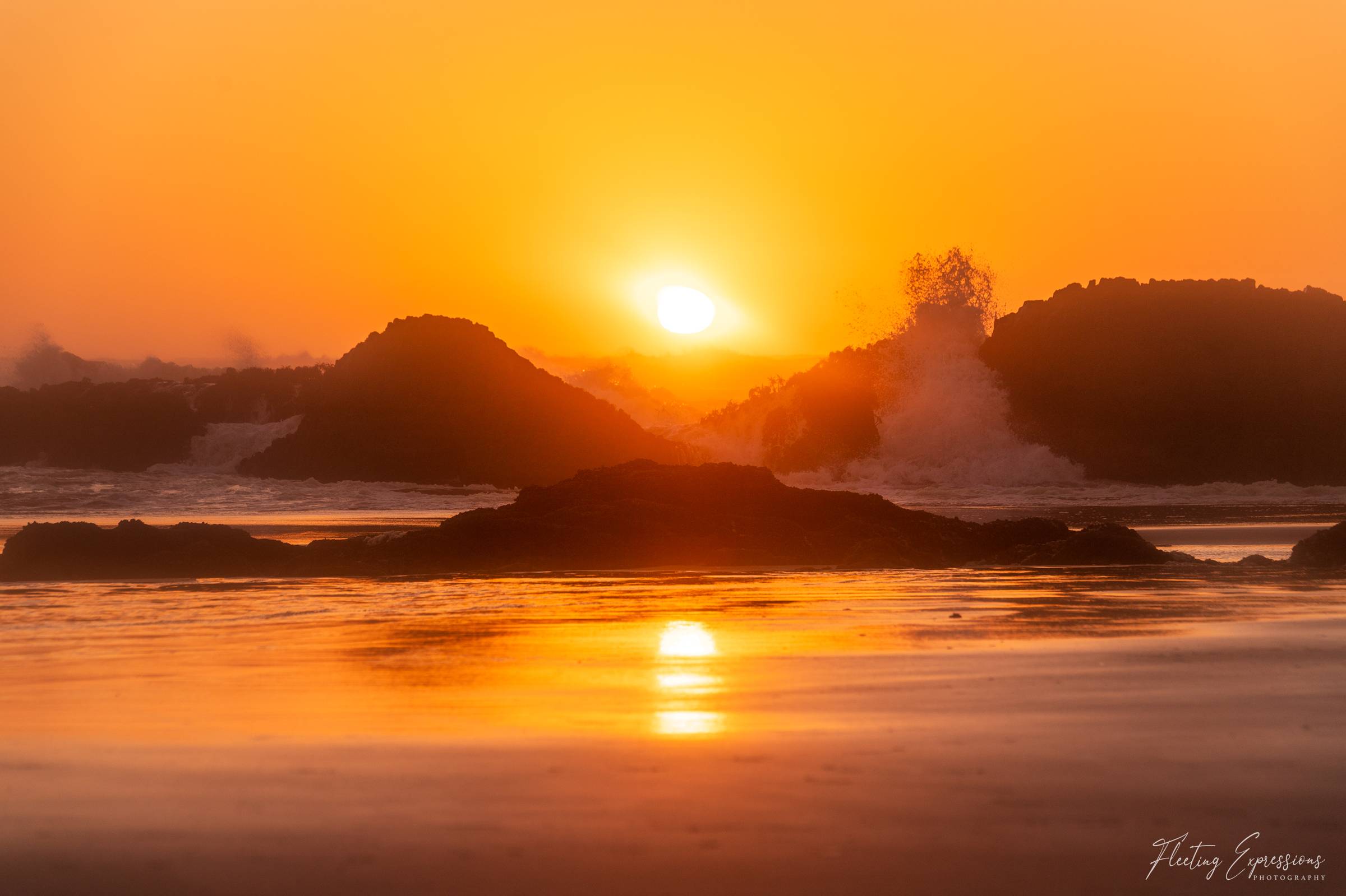 Golden sunset with sun reflected in the water and waves crashing on the rocks