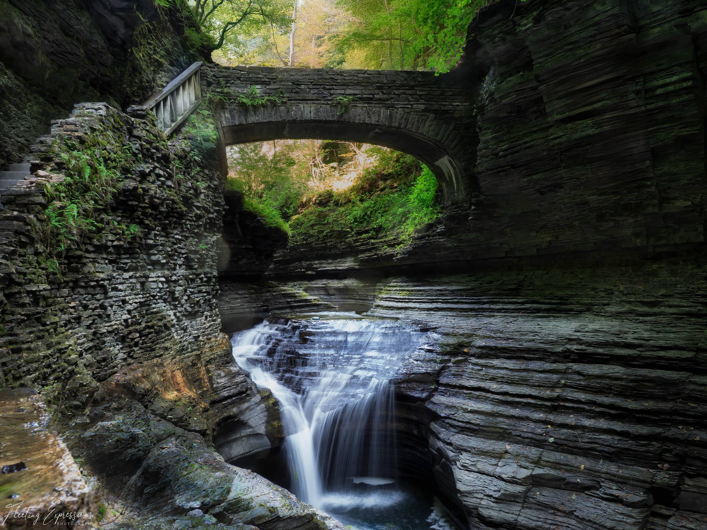 Waterfall in gorge under stone bridge with moss covered walls 