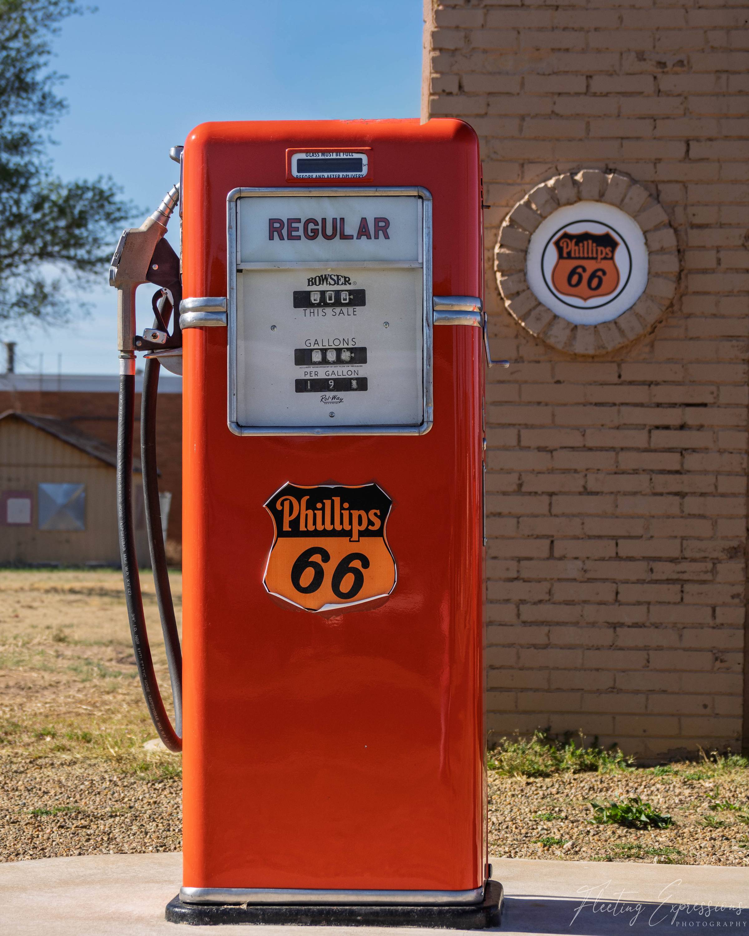 A restored bright orange vintage Phillips 66 gas pump labeled "Regular," with chrome trim and a Bowser meter, set against a tan brick wall with a round Phillips 66 logo.