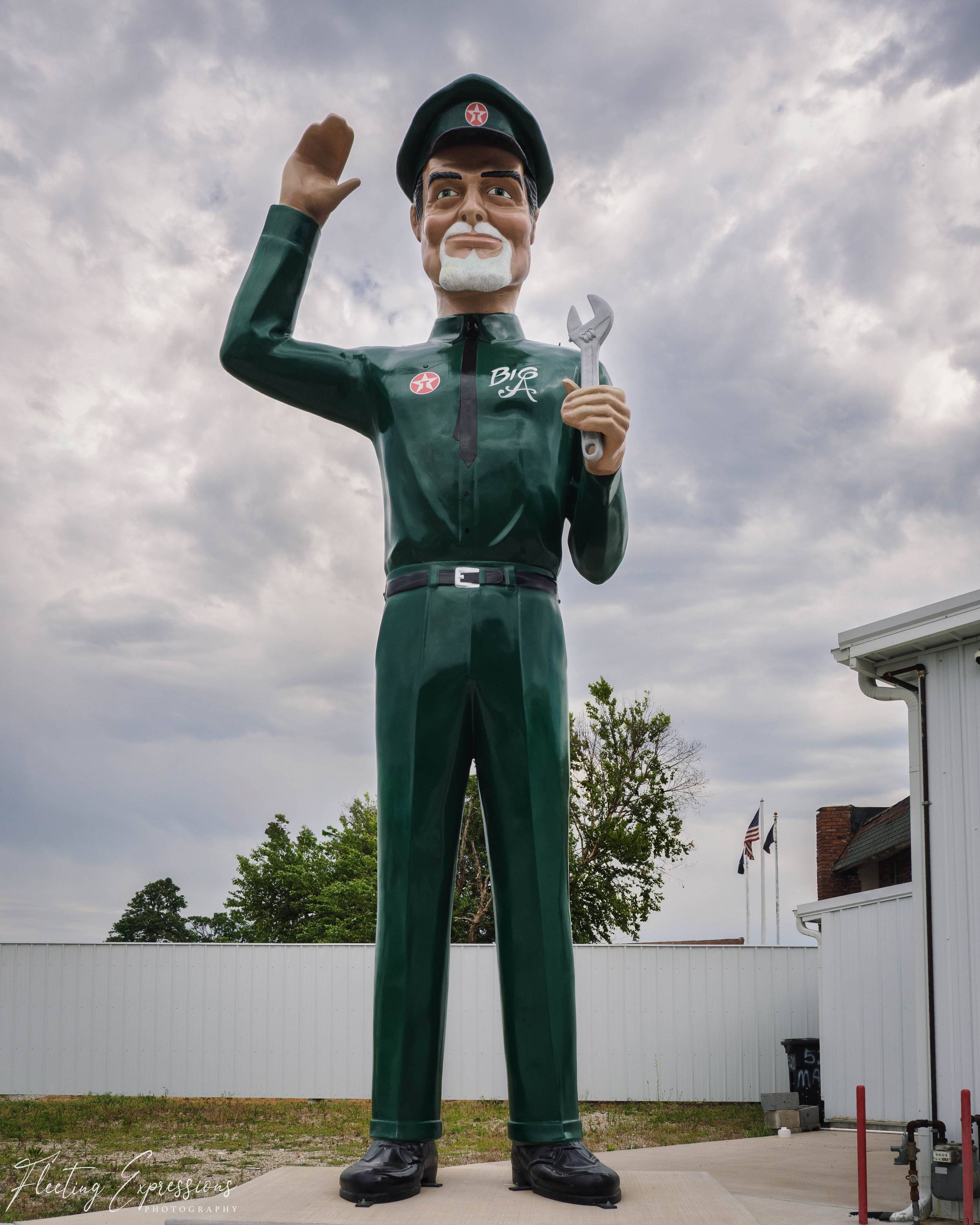 A towering green Texaco serviceman statue labeled "Big A" holds a wrench and raises one hand against a cloudy sky.