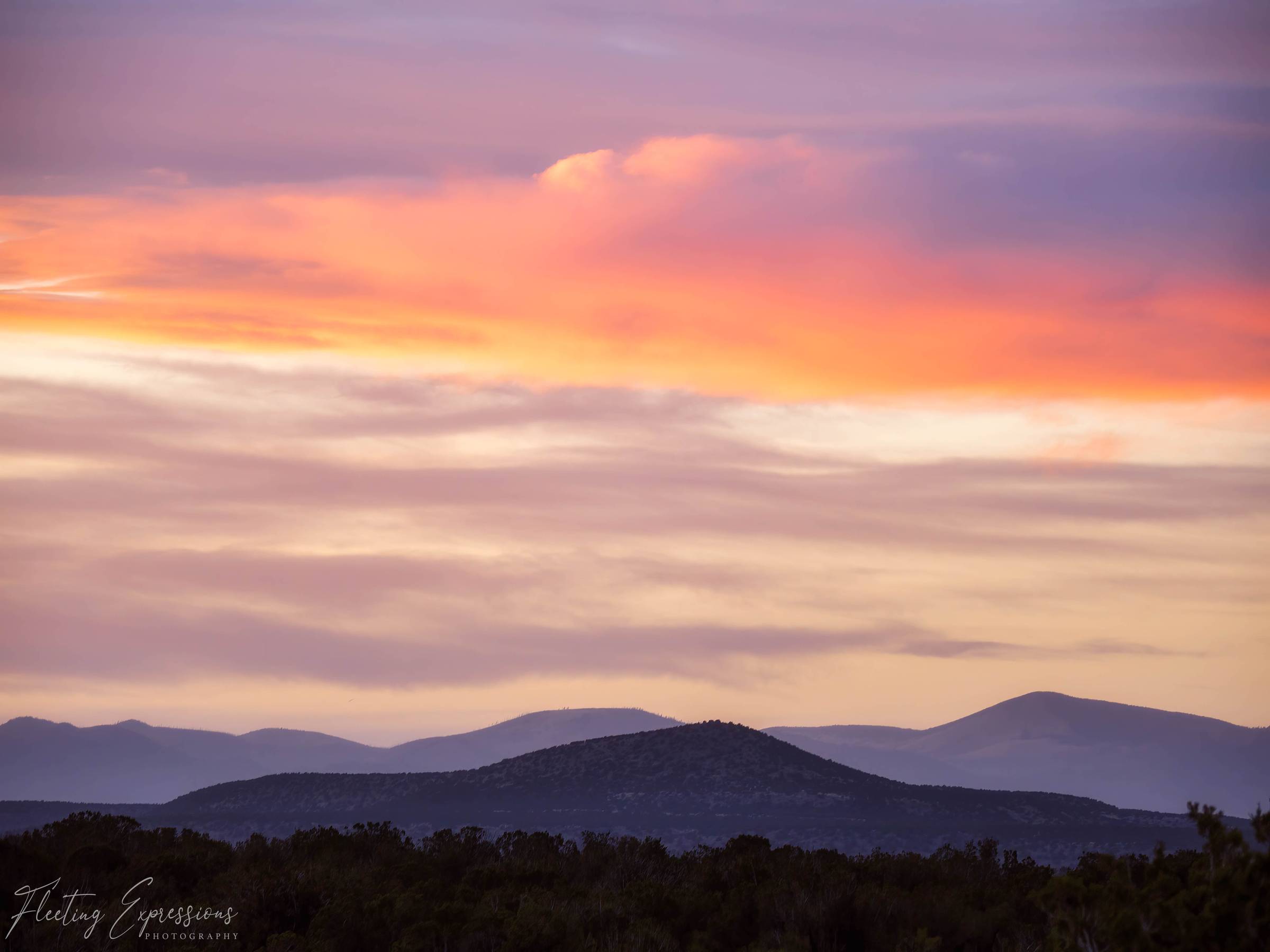 A vivid pink and orange sunset over silhouetted mountain ridges viewed from a campsite in New Mexico.