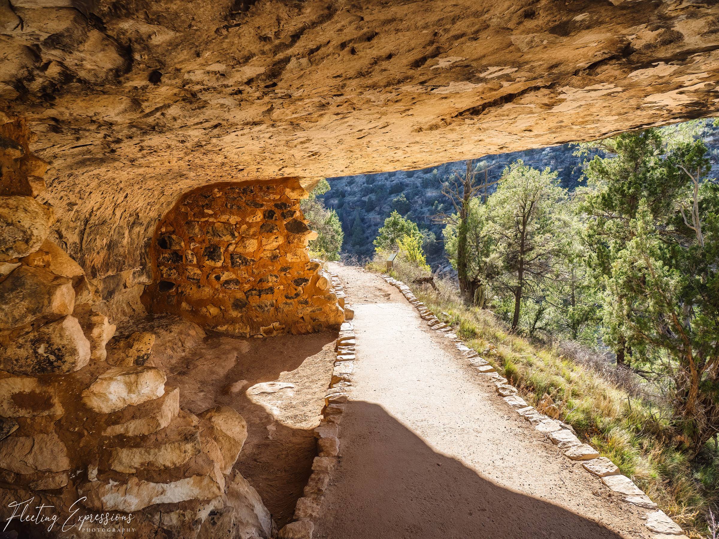 Stone pathway leading beneath an overhanging rock wall at an ancient cliff dwelling site near Flagstaff.