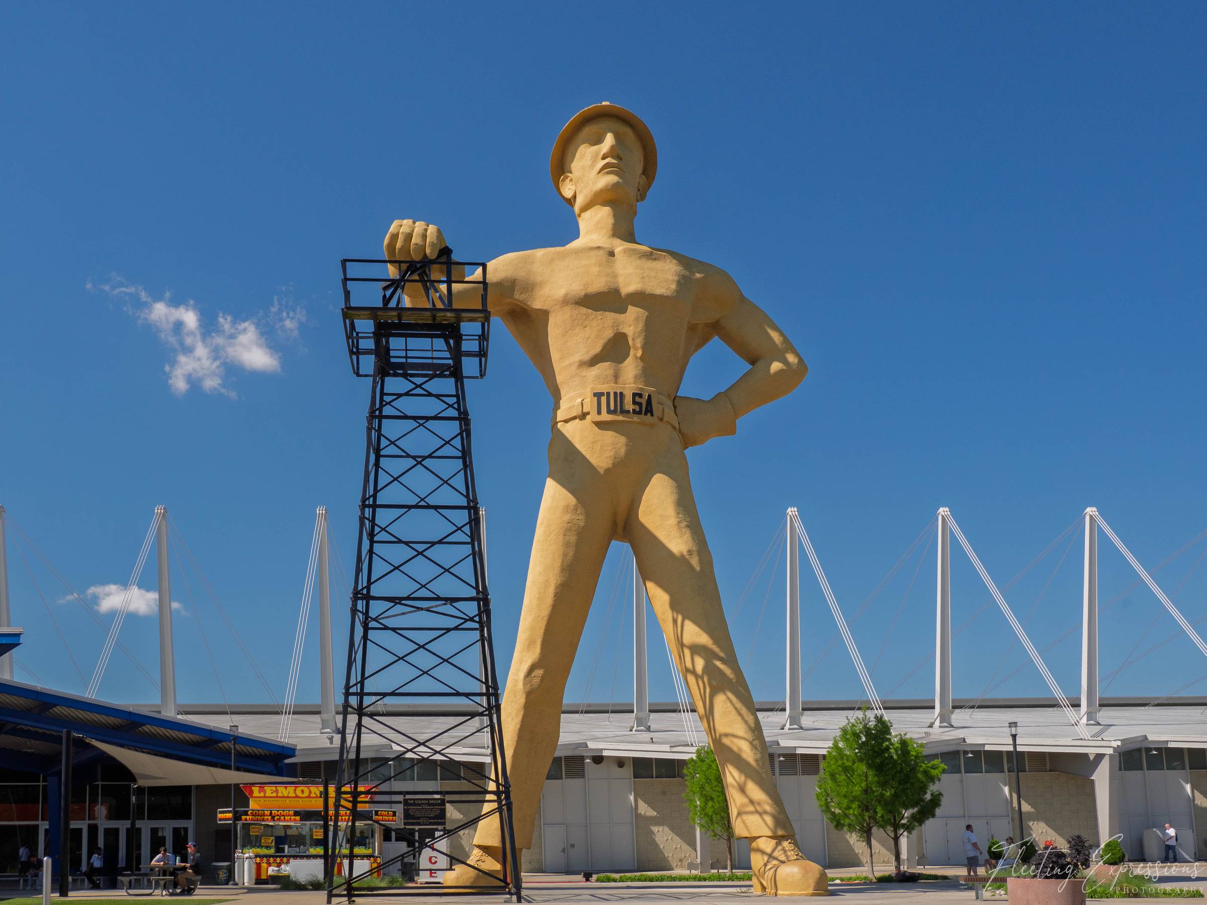 A 76-foot golden statue of a muscular oil worker in a hard hat stands with one hand resting on a steel derrick, his belt reading TULSA. 