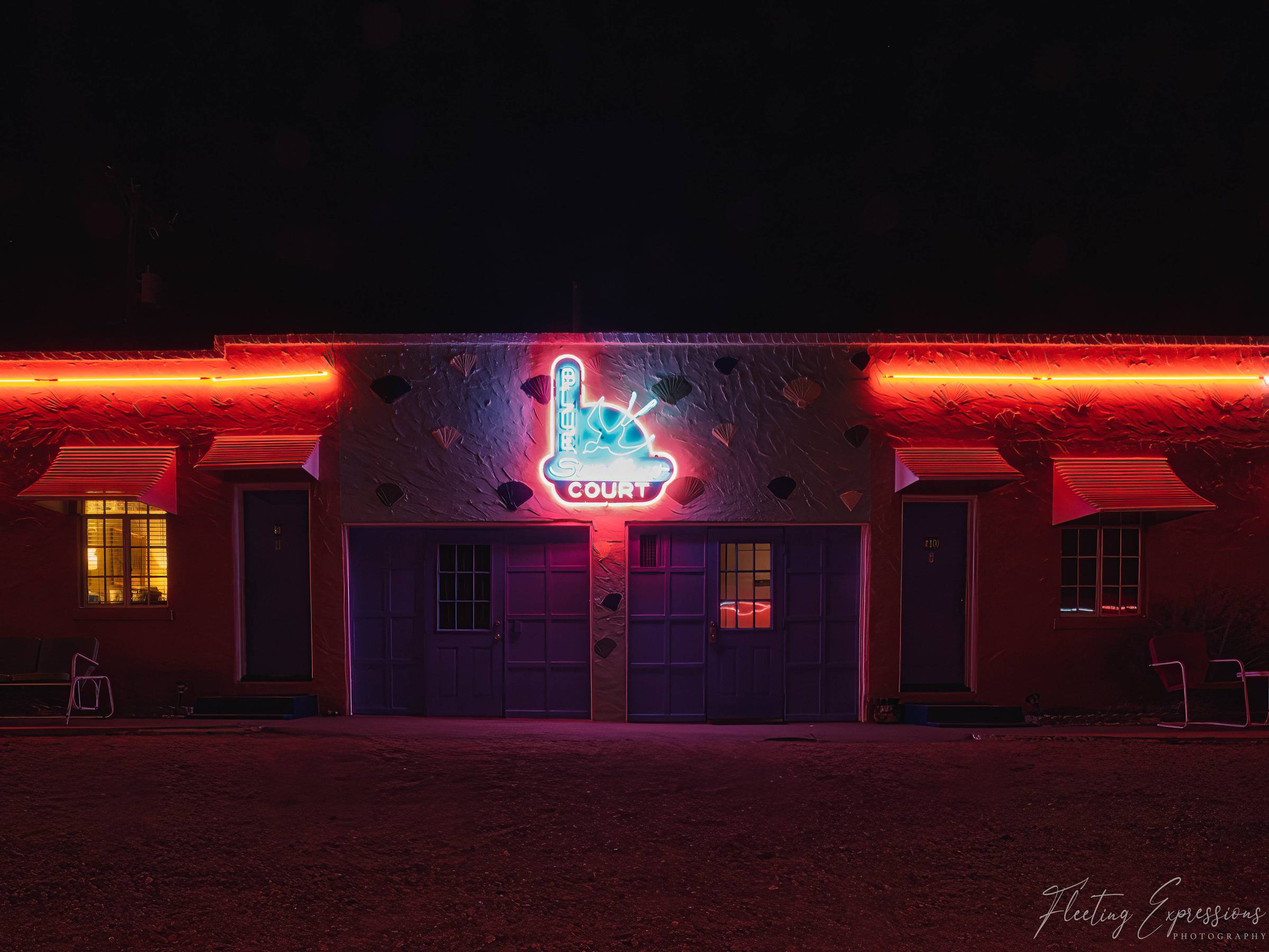 The Blue Swallow Motel at night, with red neon outlining the roofline and a blue neon "Blue Swallow Court" sign glowing above purple garage doors.