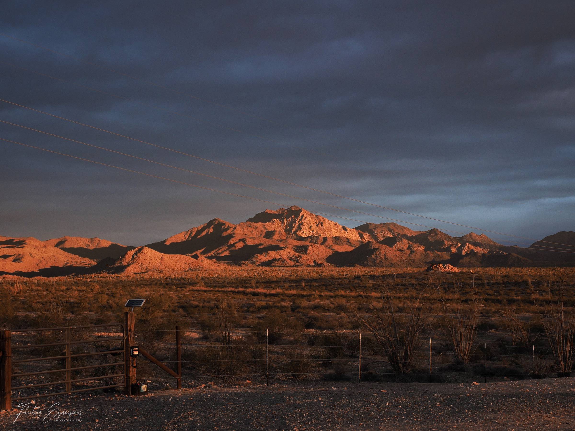 Arizona desert landscape at sunrise with golden light highlighting rocky mountain ridge and stormy skies overhead.