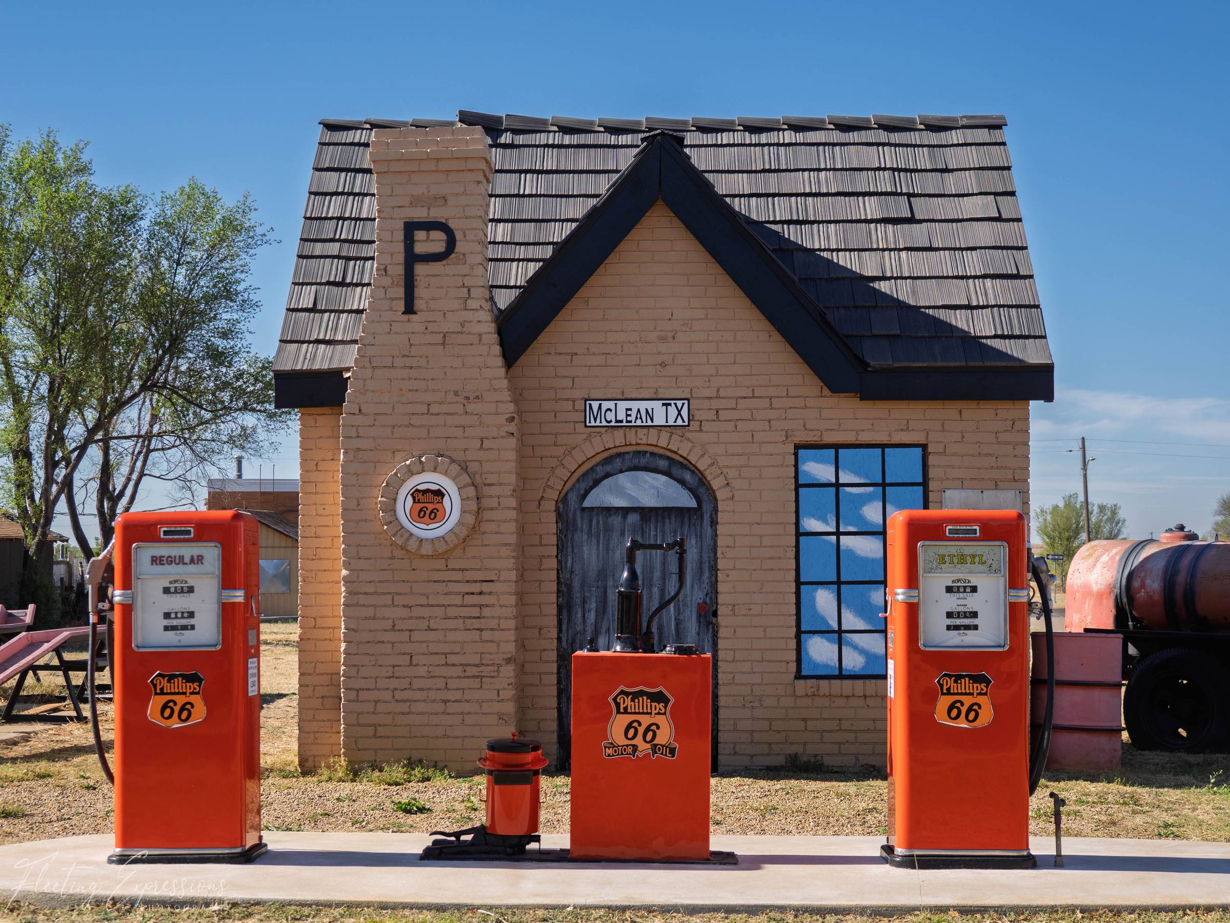 A restored cottage-style Phillips 66 gas station in McLean, Texas, with three bright orange vintage pumps lined up in front of a tidy brick building.