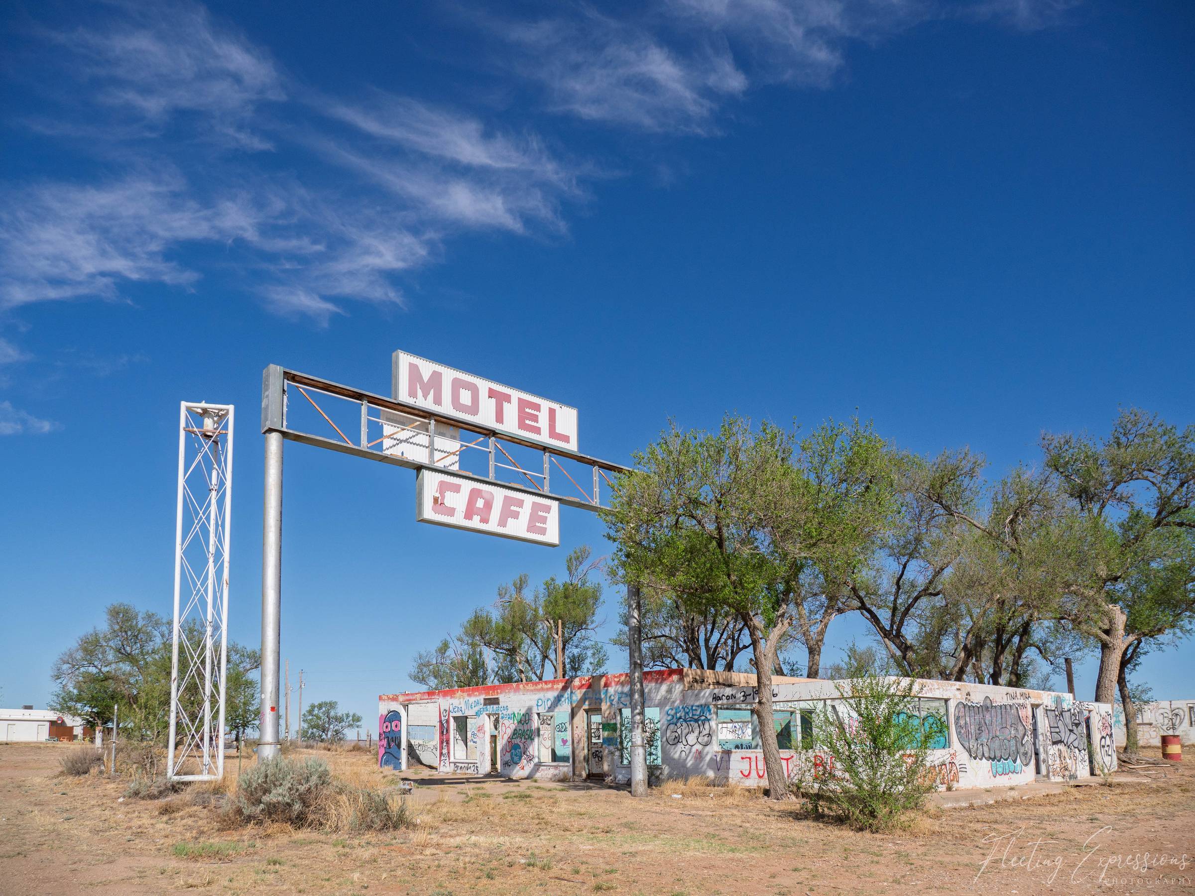 An abandoned motel and cafe in Glenrio, Texas, with faded pink signs still hanging above graffiti-covered walls under a wide blue sky.