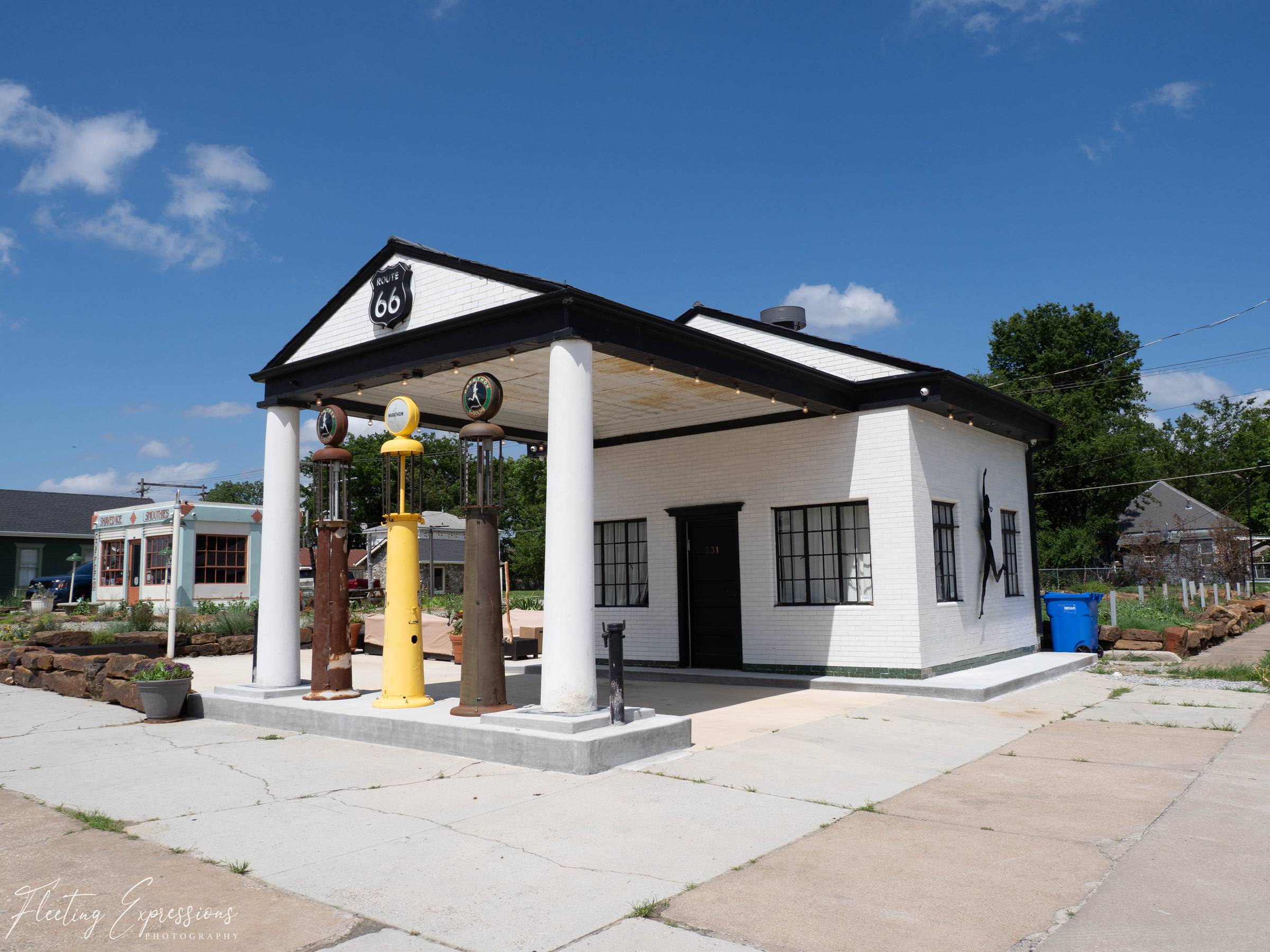 Restored historic Route 66 filling station in Miami, Oklahoma, featuring white columns, vintage gas pumps, and a bright blue summer sky.