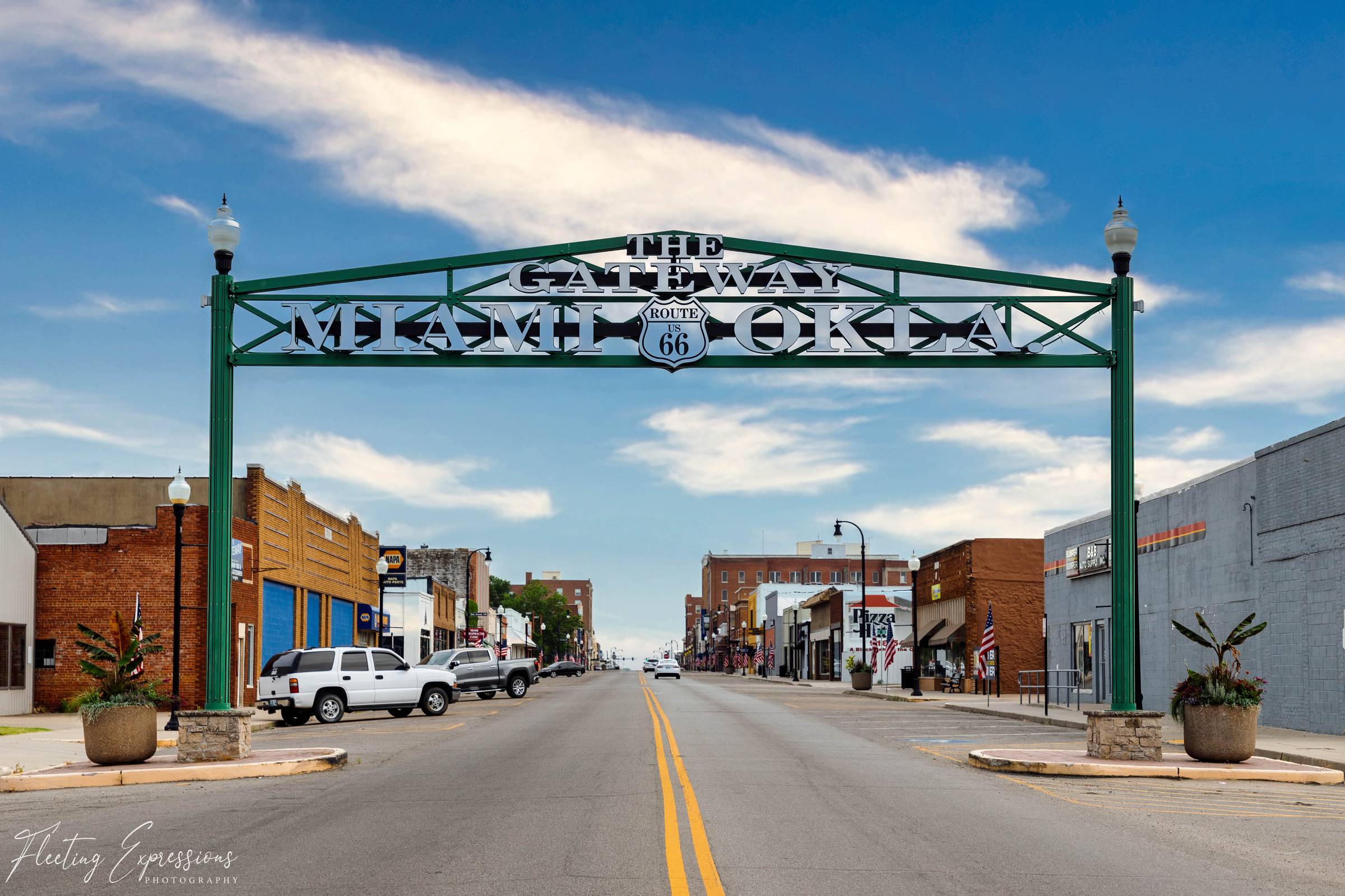 The Gateway to Miami, Oklahoma arch spans historic Route 66 over a wide downtown street lined with local businesses and American flags.
