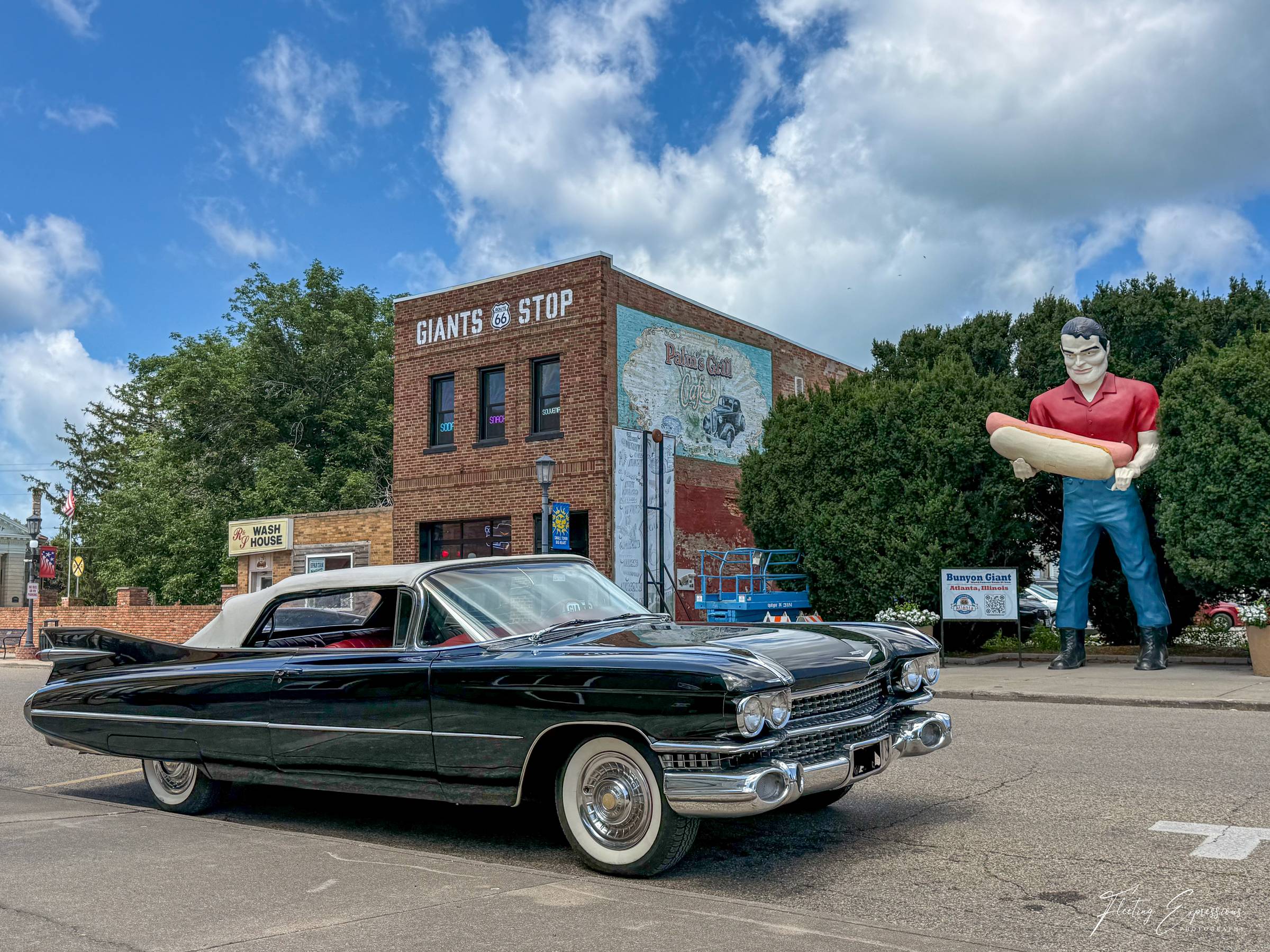 A black 1959 Cadillac convertible parks in front of the towering Bunyon Giant holding a hot dog in Atlanta, Illinois.