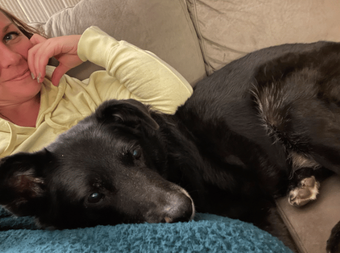 Preview image of a girl in a yellow hoodie with her black dog curled up on her lap.