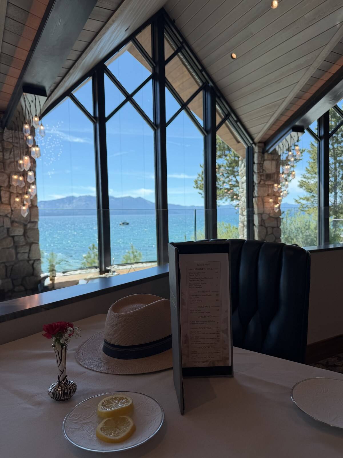 Afternoon tea table at The Edge, Edgewood Tahoe — lemon slices and a Panama hat in front of tall windows framing Lake Tahoe and the Sierra.