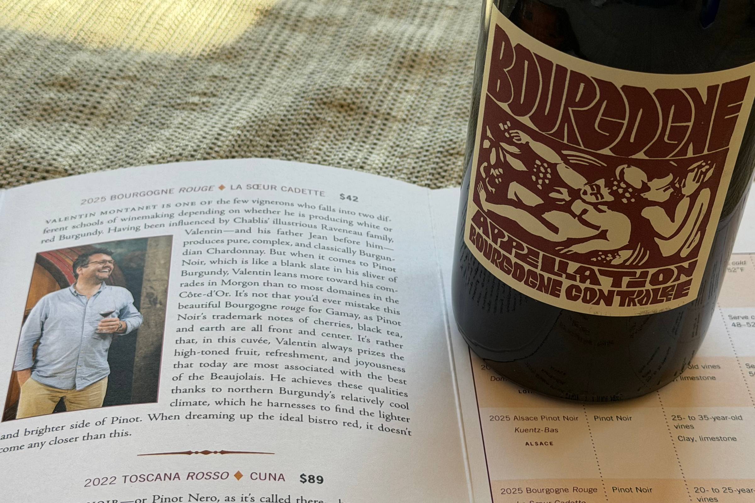 A bottle of La Sœur Cadette Bourgogne Rouge standing on an open Kermit Lynch Club Chevalier newsletter, with the winemaker's photo and write-up visible on the page.