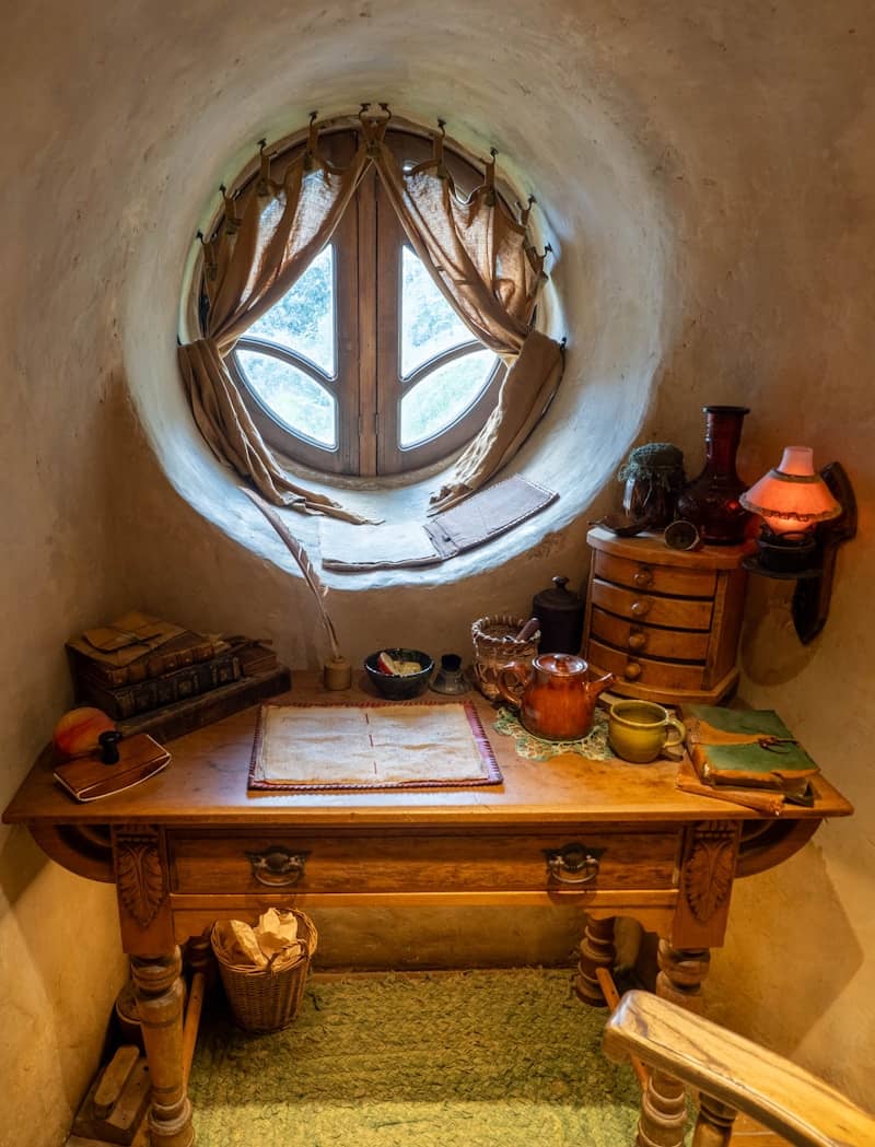 Wooden desk with books and teapot by round window.