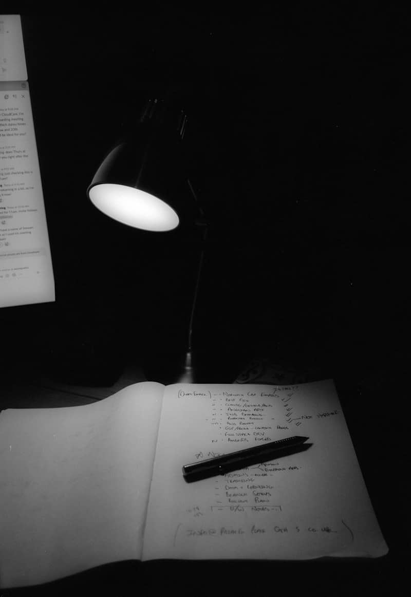 A lit desk lamp illuminates a notebook and pen.