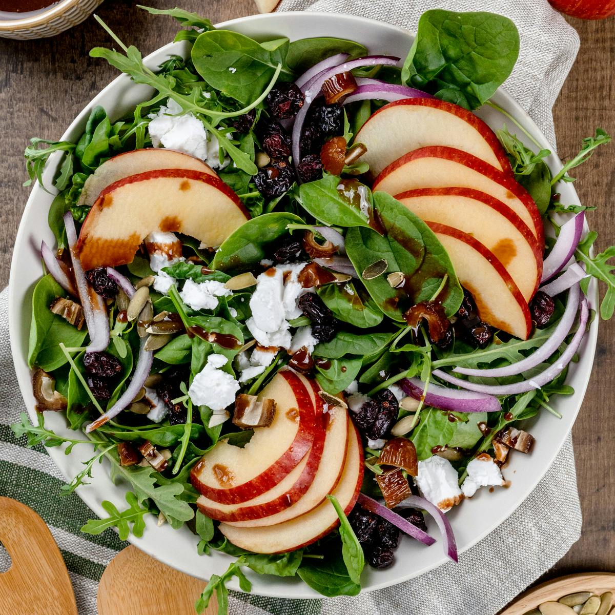 Close up of a big bowl filled with an arugula and fuji apple salad with balsamic dressing. 
