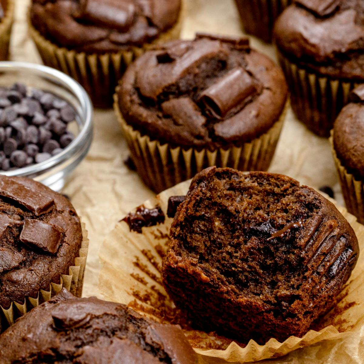 Many chocolate protein muffins on crinkled brown parchment paper. 