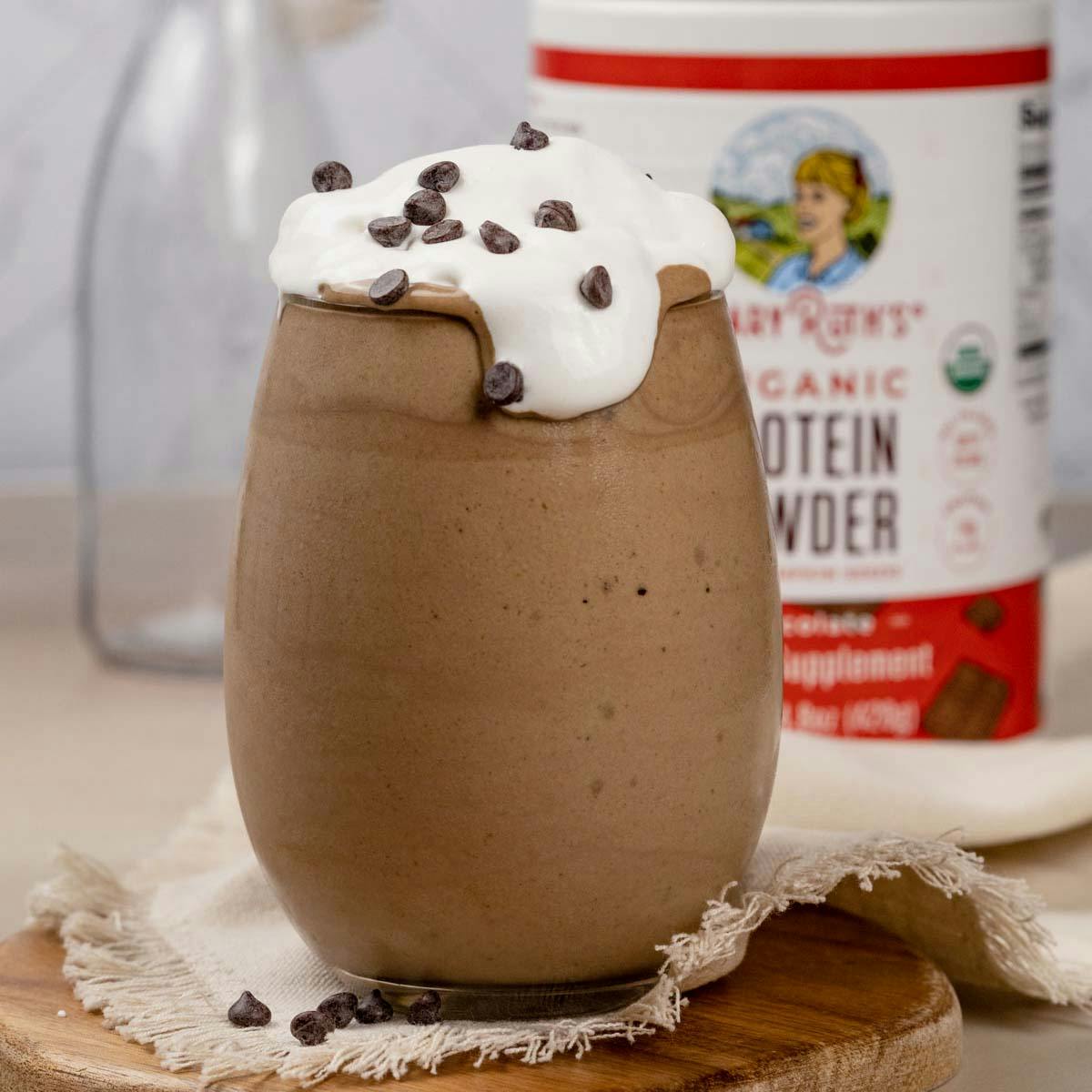 A glass filled with nut butter banana chocolate protein shake with whipped cream and mini chocolate chips on top. 