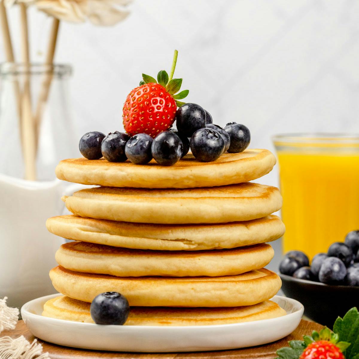 A stack of protein pancakes on a white plate with fresh berries. 