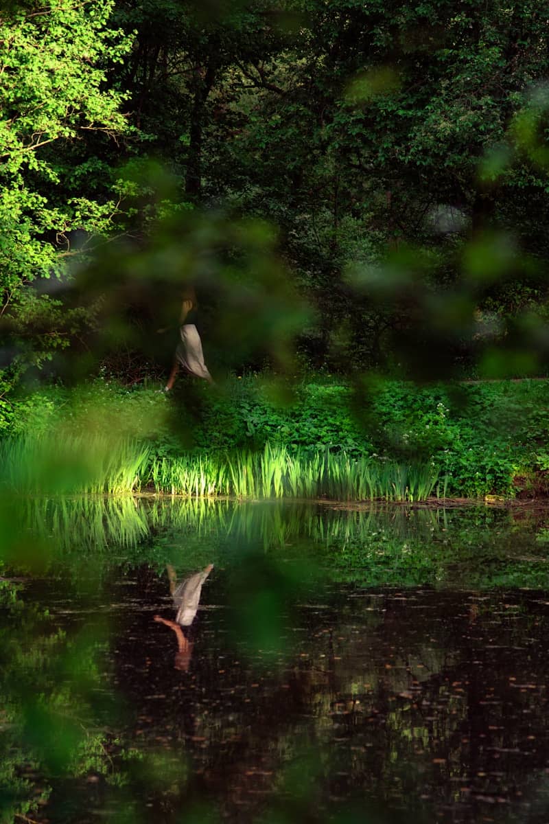 A person in a light skirt walking along a pond reflecting in the water.