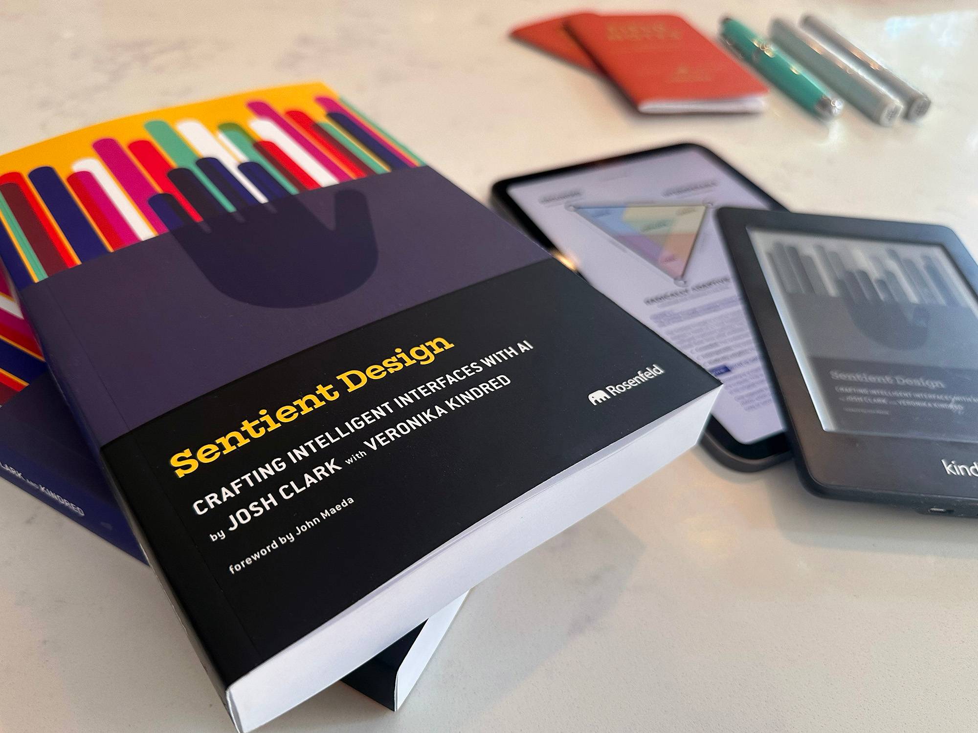 Sentient Design paperbacks next to Kindle and iPad editions on a marble surface