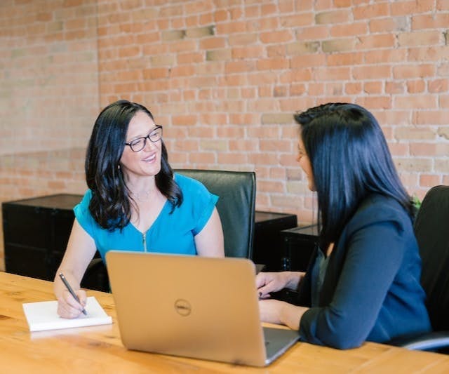 woman in teal t-shirt sitting beside woman in suit jacket