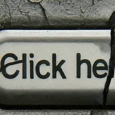 A faded and cracked "Click here" webpage button atop a gray fissured background.