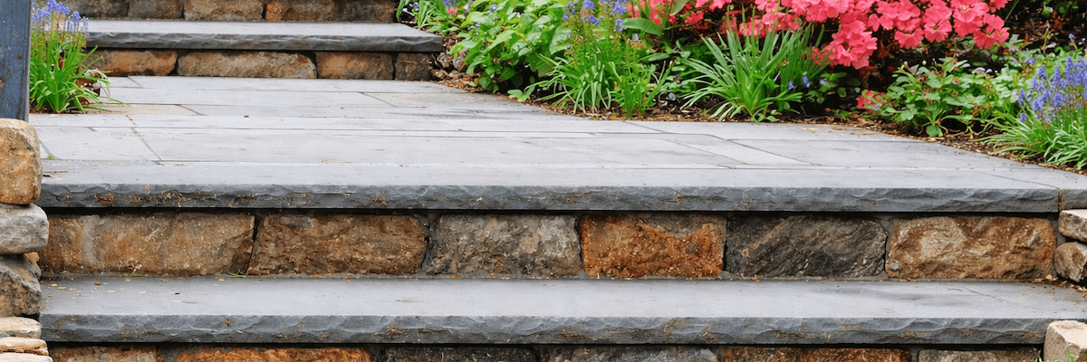 Close up of stone steps with a flat terrace between two flights enclosed by bushes and brightly colored flowers