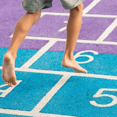 A boy's legs skip across the numbered squares of a pink and blue hopscotch board