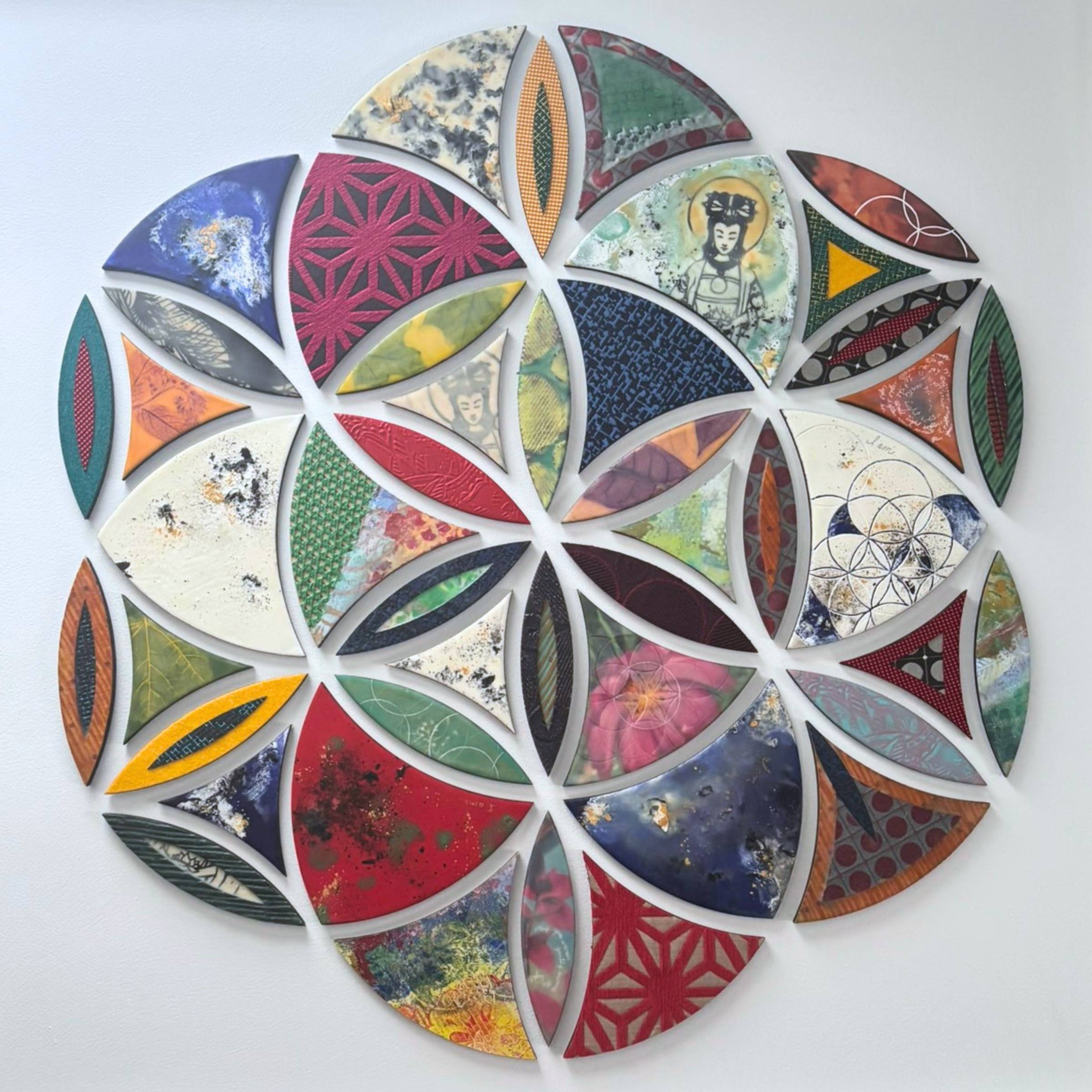 A large square framed panel displaying the Seed of Life geometric pattern, composed of dozens of individual encaustic panels in varied colors and textures. Each panel features unique layered wax surfaces in deep reds, blues, greens, golds, and earth tones