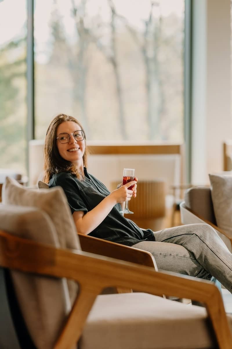 A woman in glasses sips wine in a lounge chair.