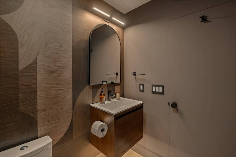Modern bathroom with a wooden vanity and arched mirror.