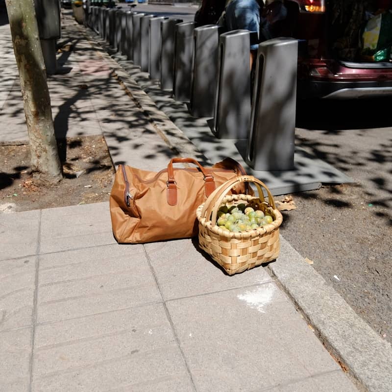A duffel bag and basket of grapes on pavement.