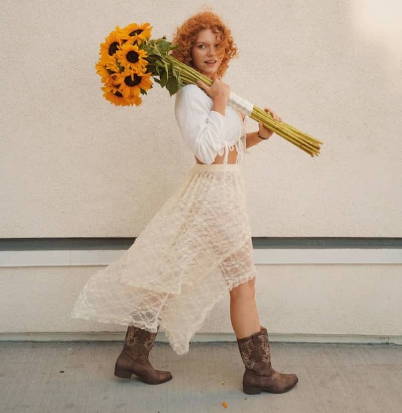 Woman with red curly hair carrying sunflowers