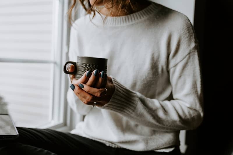 A woman holding a cup of coffee while looking at her laptop