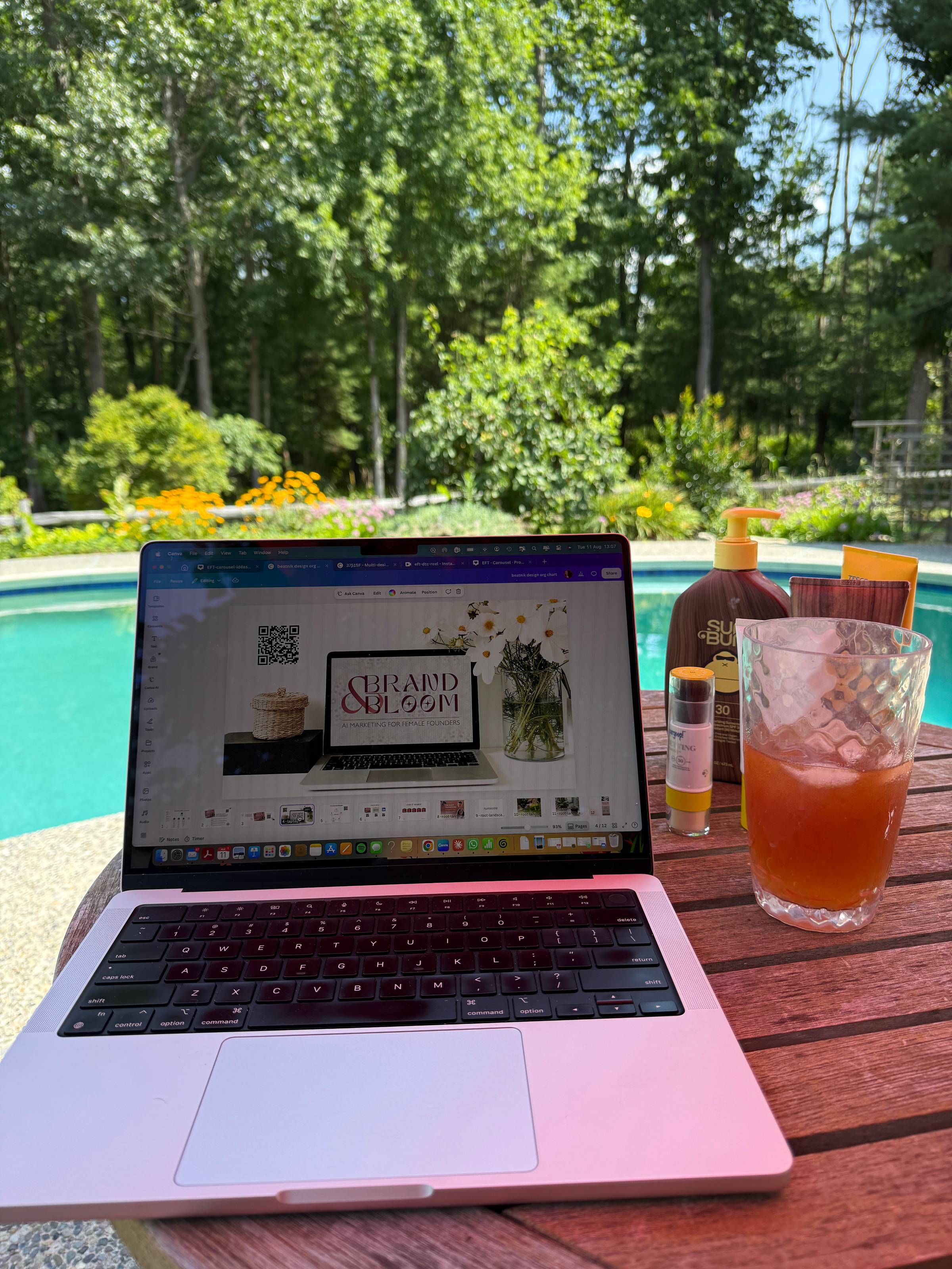 laptop on a table with a drink next to it, overlooking a pool