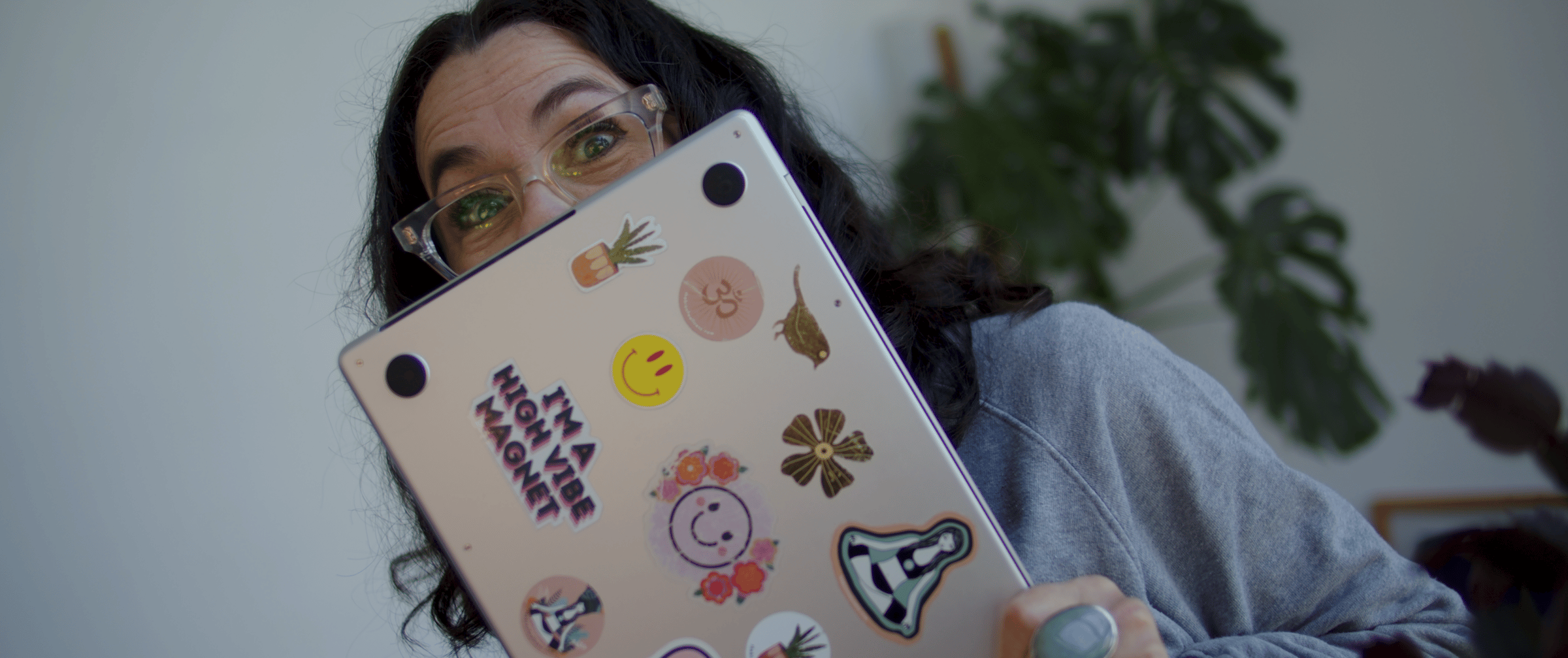 woman with dark hair and clear glasses holding a laptop with stickers on the back of it.