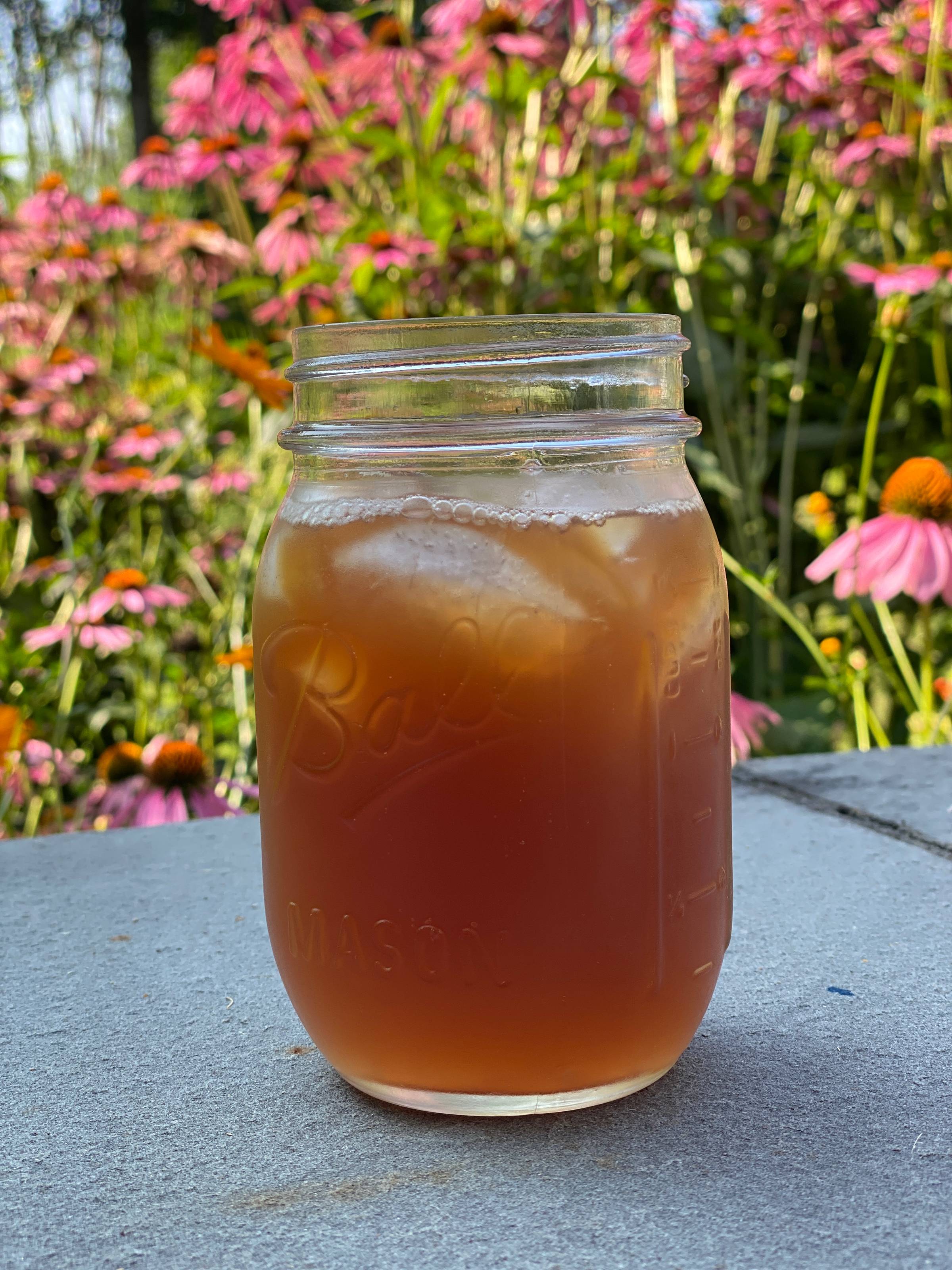 A glass of ice tea mixed with lemonade on a table with pink flowers in the background.