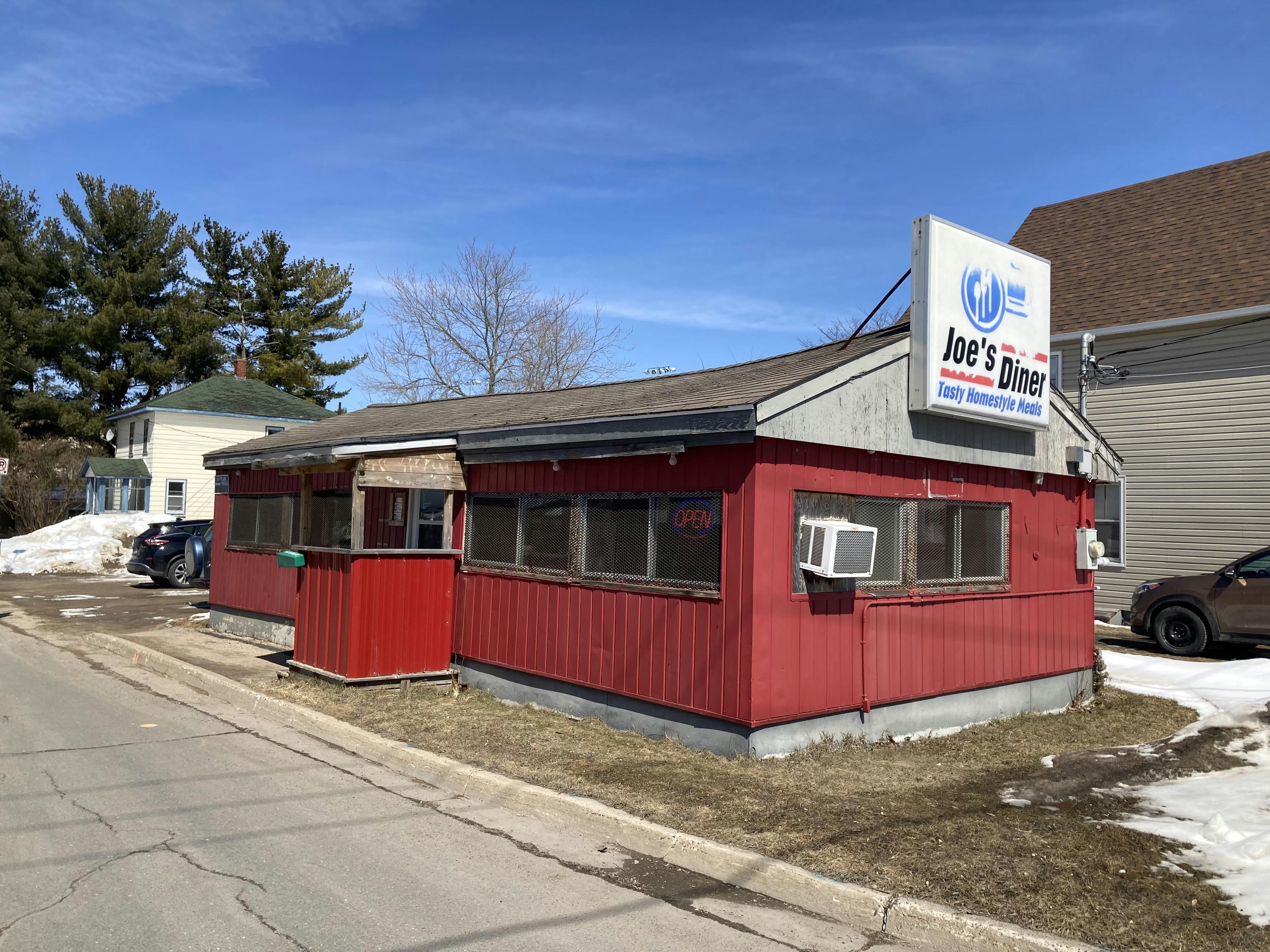 A photo of a red, one-storey classic 50s or 60s diner with a faded white and blue and red sign